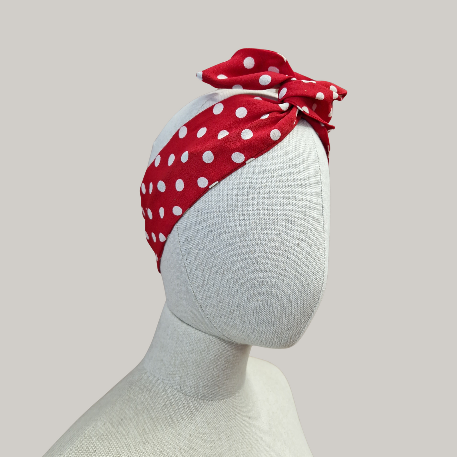A red headband with white polka dots, displayed on a mannequin head.