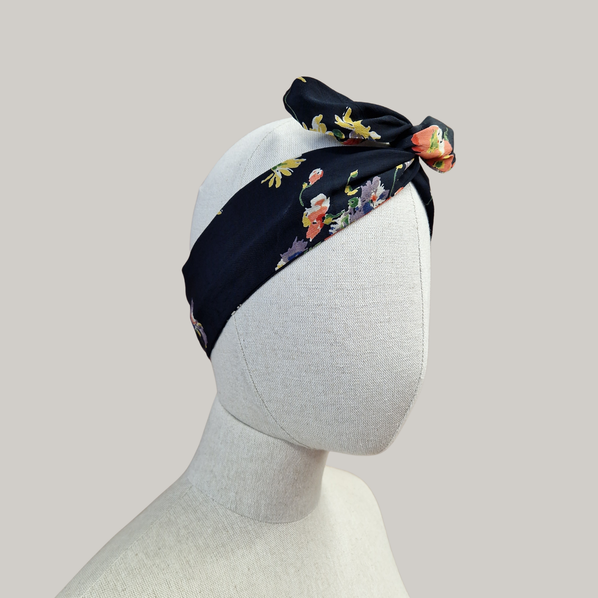 A black floral headband displayed on a mannequin head.