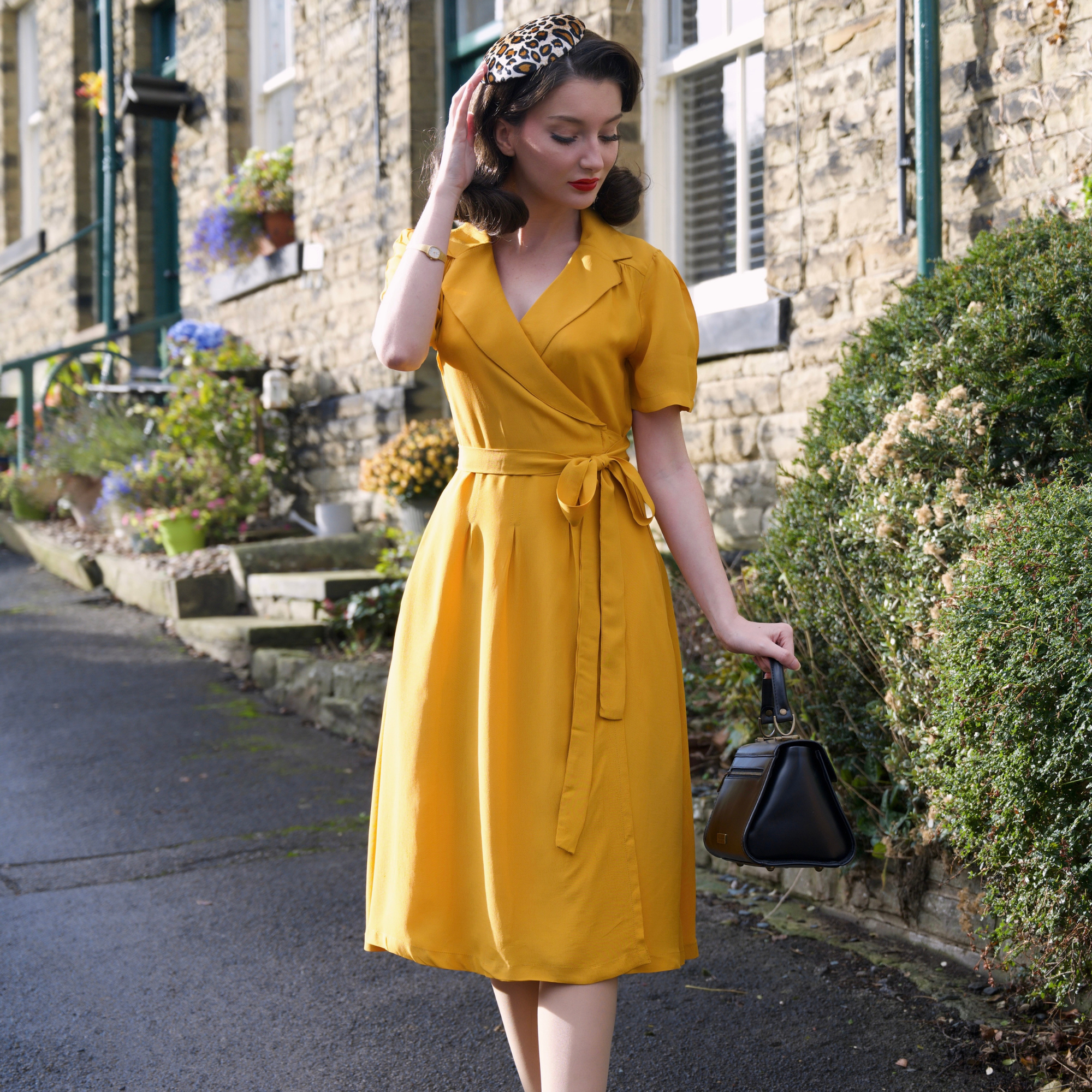 Woman in a yellow dress standing on a street with a stone building in the background