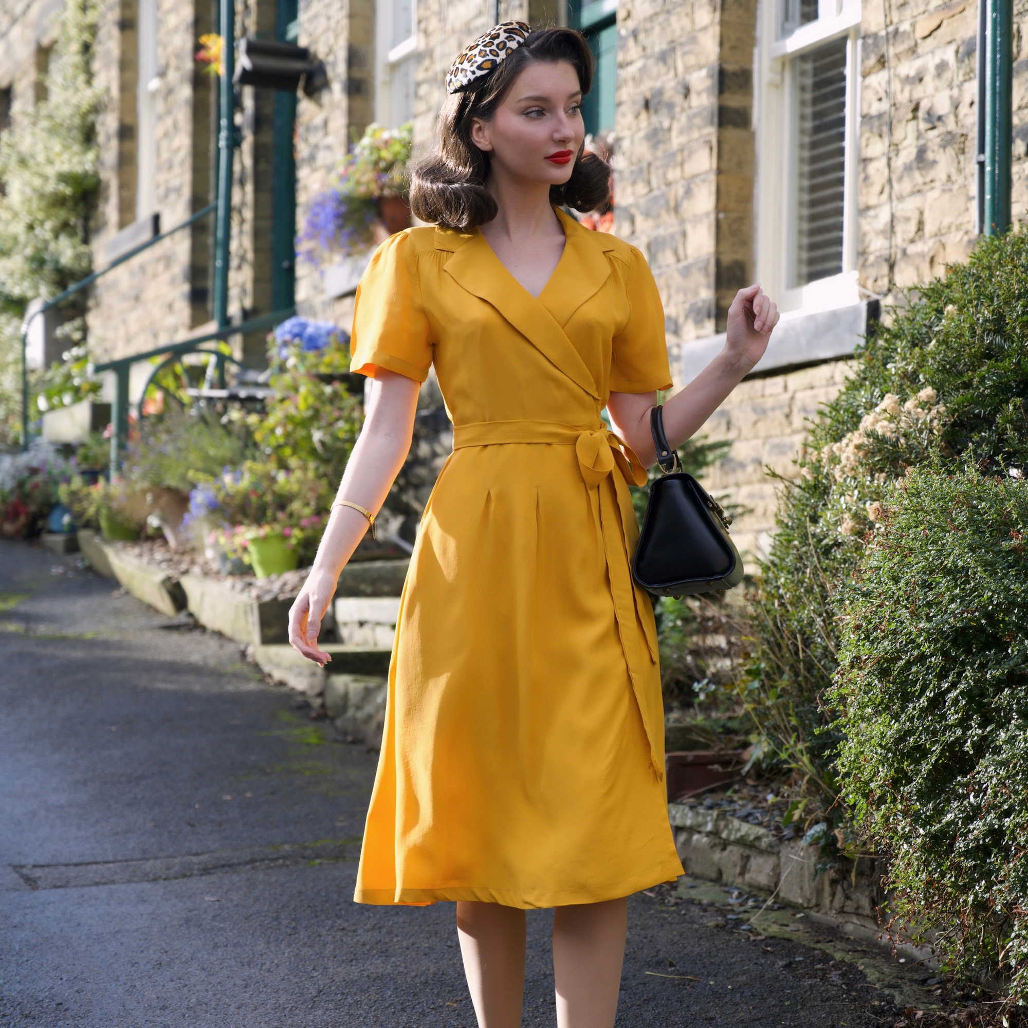 Woman in a yellow dress standing outdoors with a stone building and garden in the background