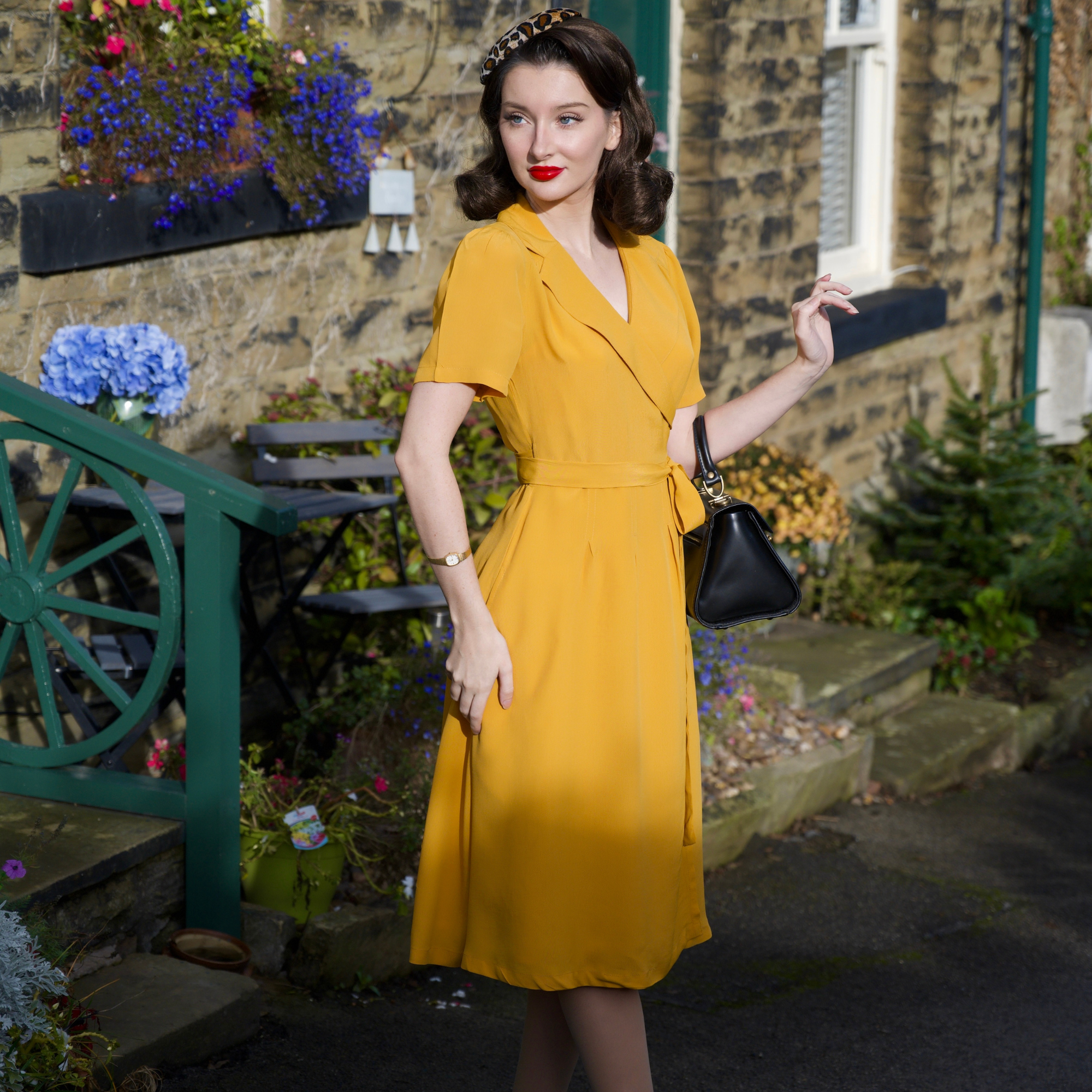 Woman in a yellow dress standing outdoors with flowers and a building in the background