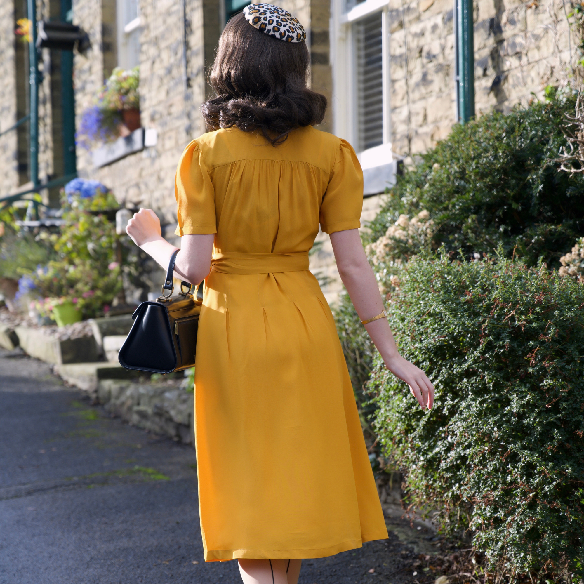 Woman in a yellow dress walking down a street with stone buildings and greenery.