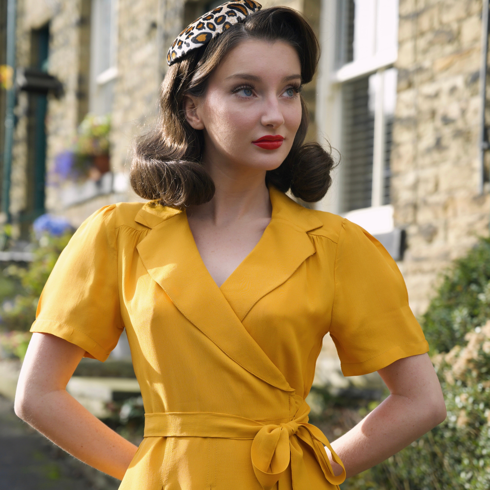 Woman in a yellow dress with a leopard print headband standing outdoors.