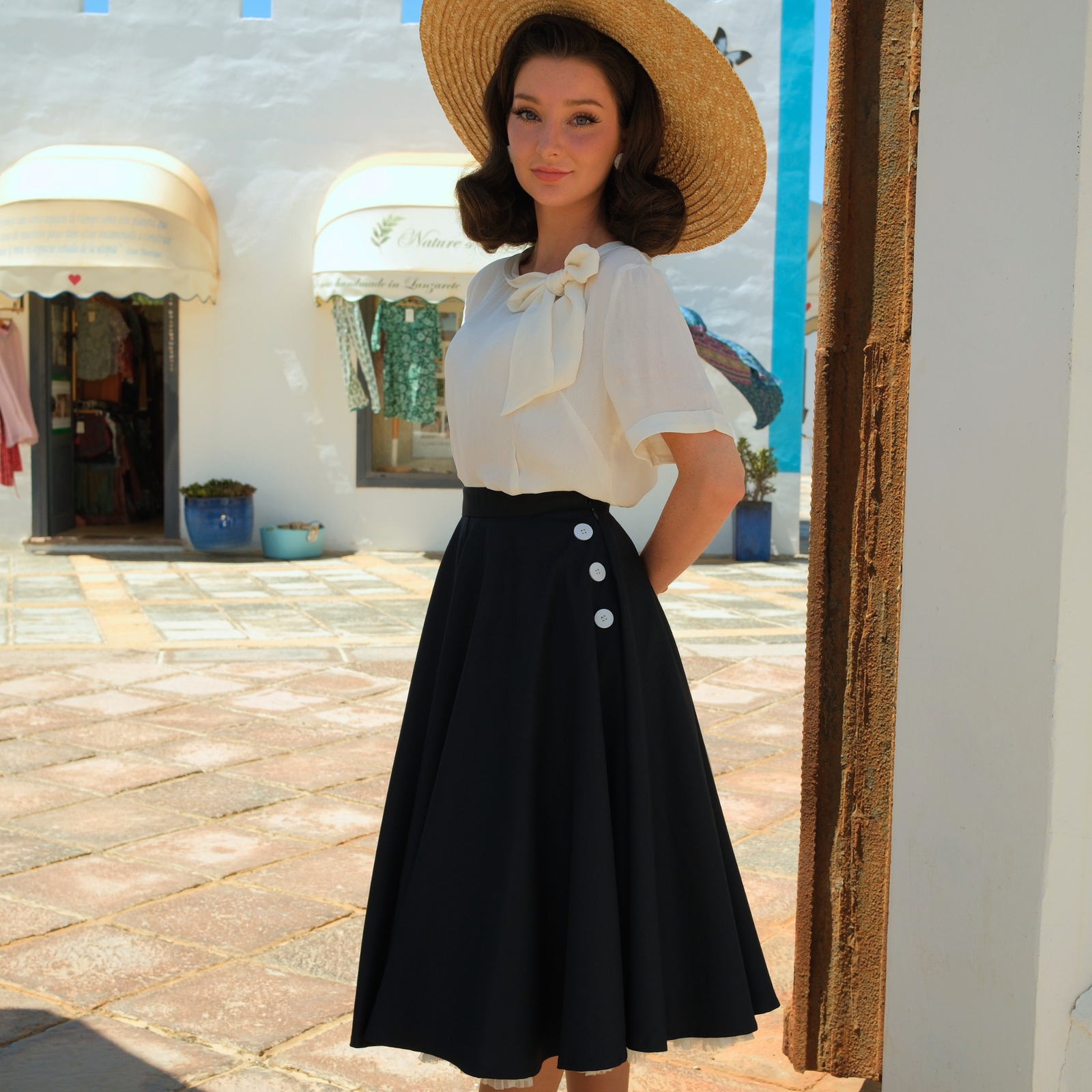 Woman wearing a navy skirt and cream blouse in front of a white building.