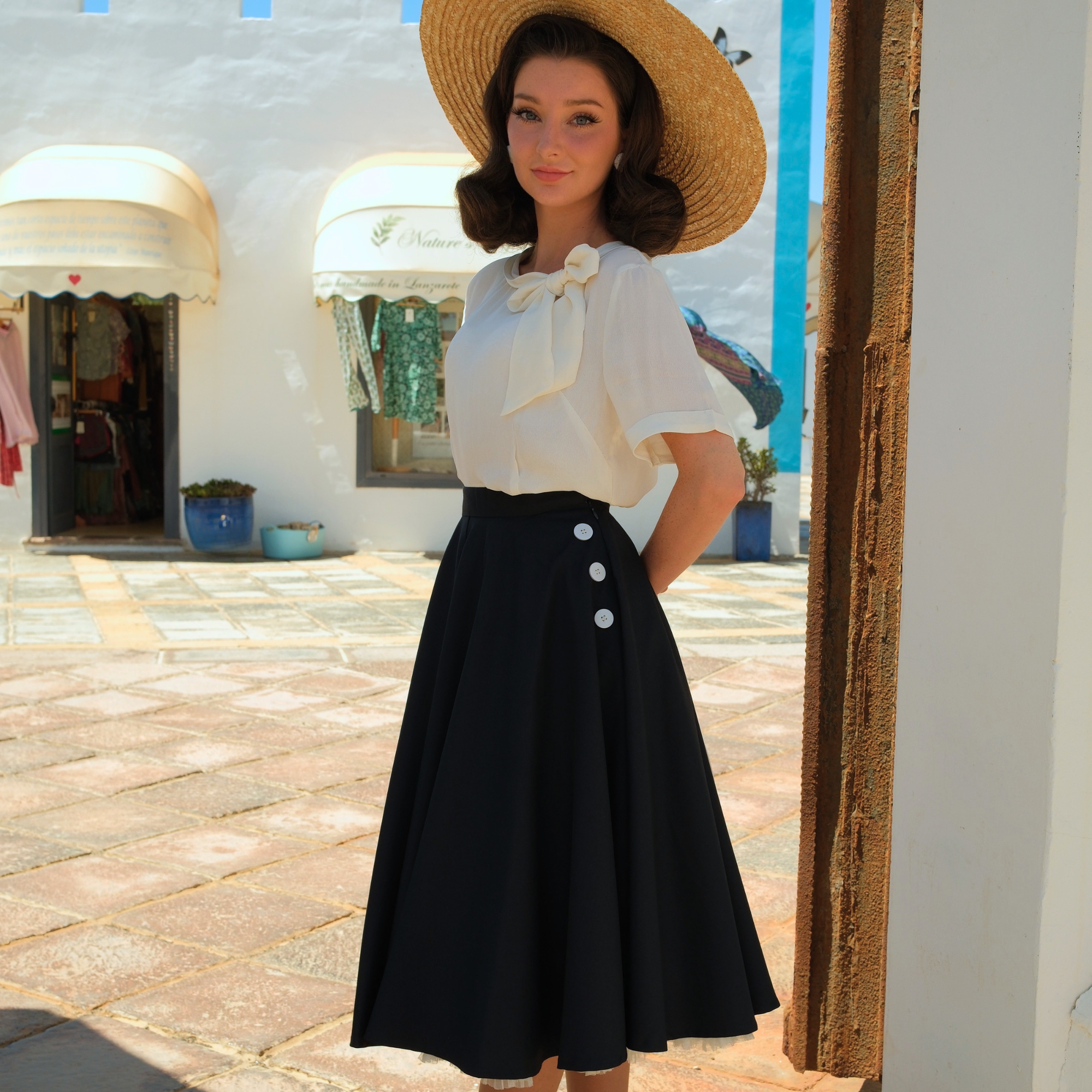 Woman wearing a navy skirt and cream blouse in front of a white building.