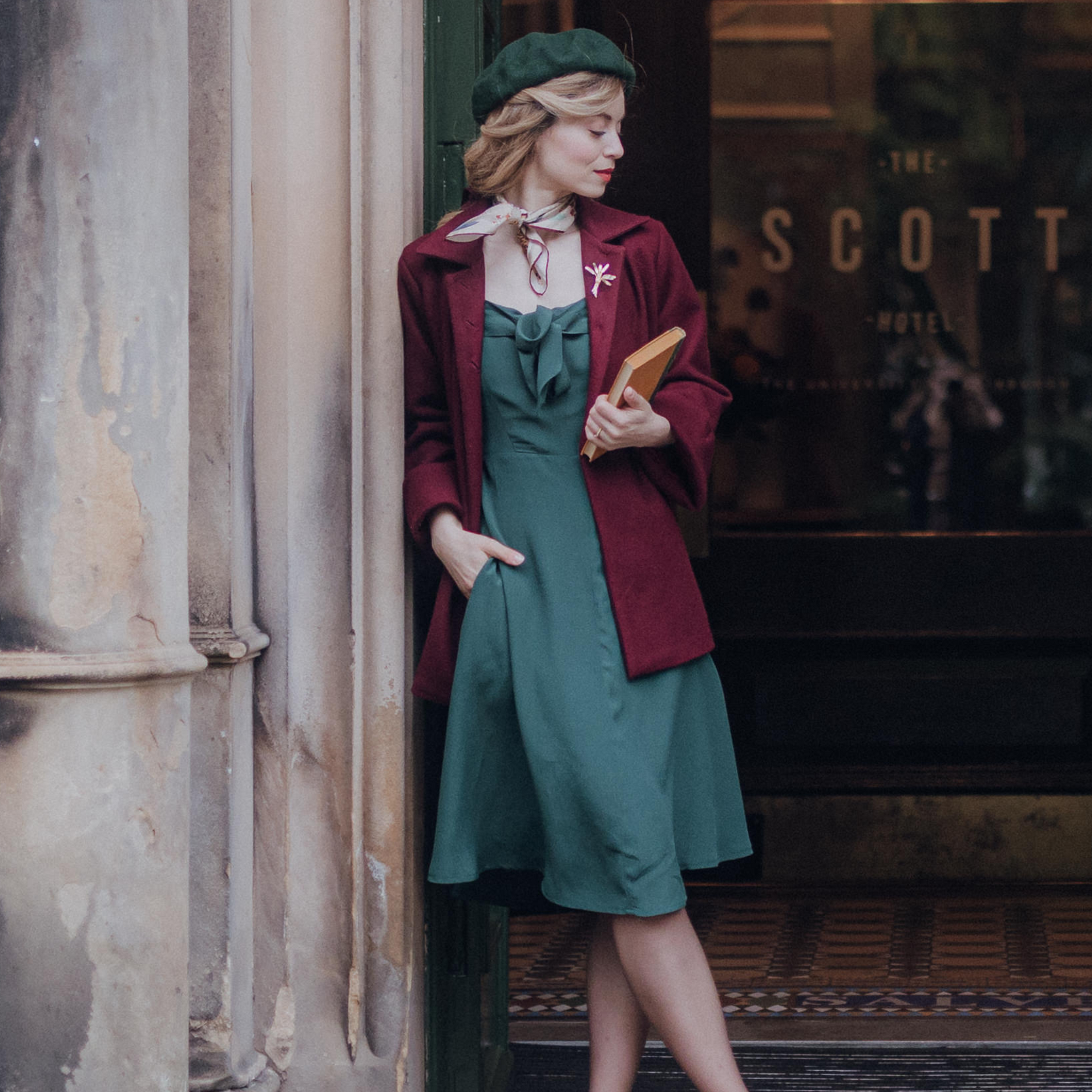 A woman wearing a vintage style swing jacket in wine color, with big turn-back cuffs and 3 big buttons at the front, paired with a green dress.
