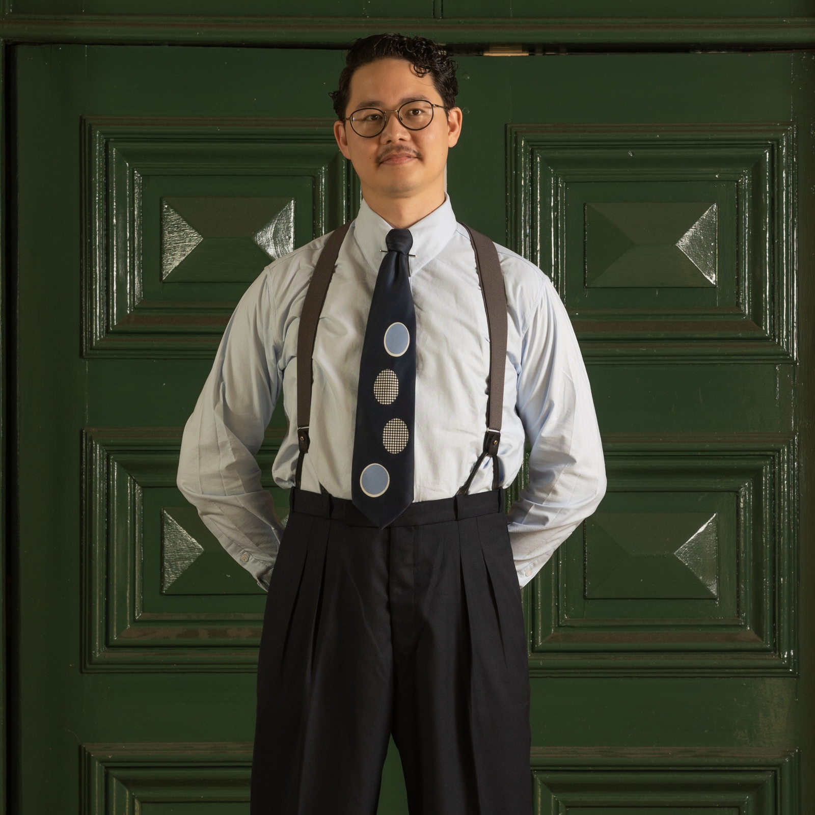 Man wearing suspenders and a patterned tie against a green door background
