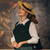 Model wears a 1940s style cable knitted slipover/vest in dark green with a v-neck neckline with a cream long sleeve Jacqui blouse underneath, paired with a straw boater style hat. 