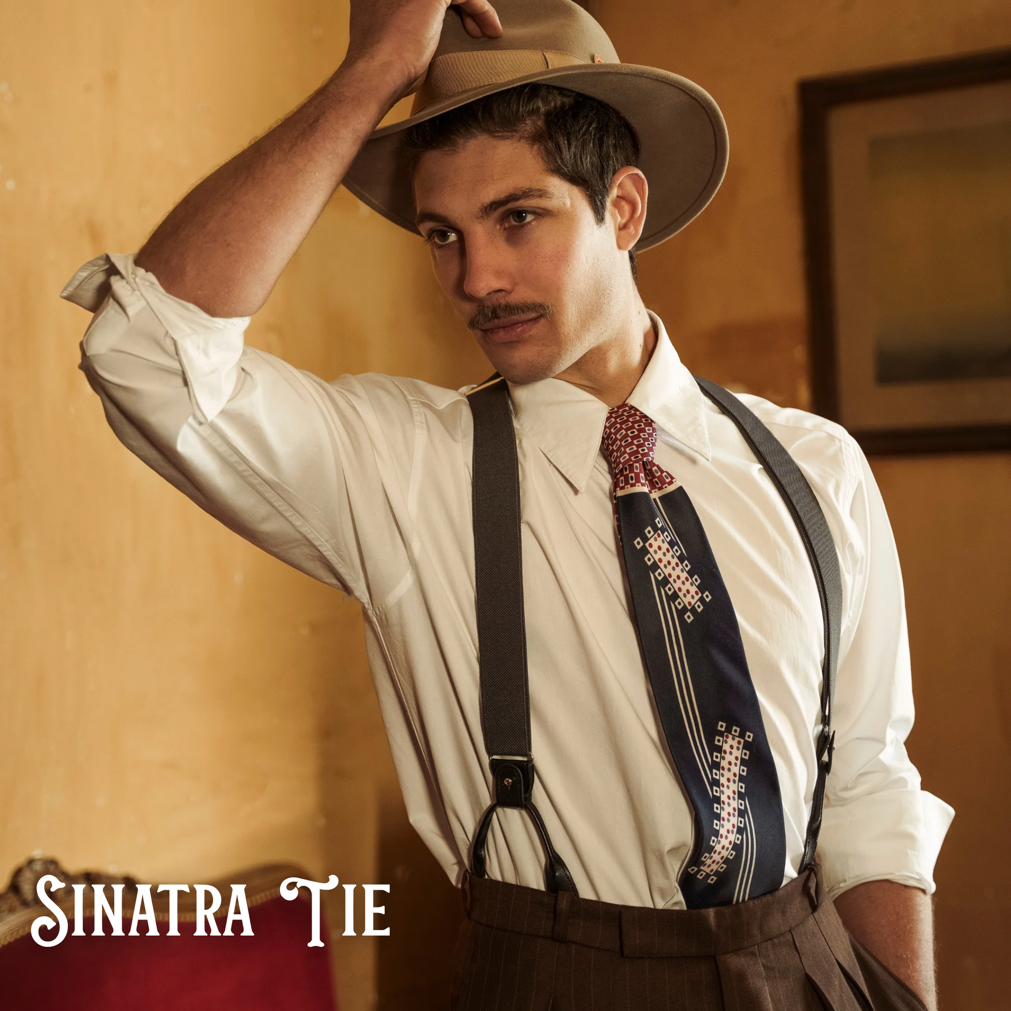 Man wearing a vintage outfit with suspenders and a tie, holding a hat.