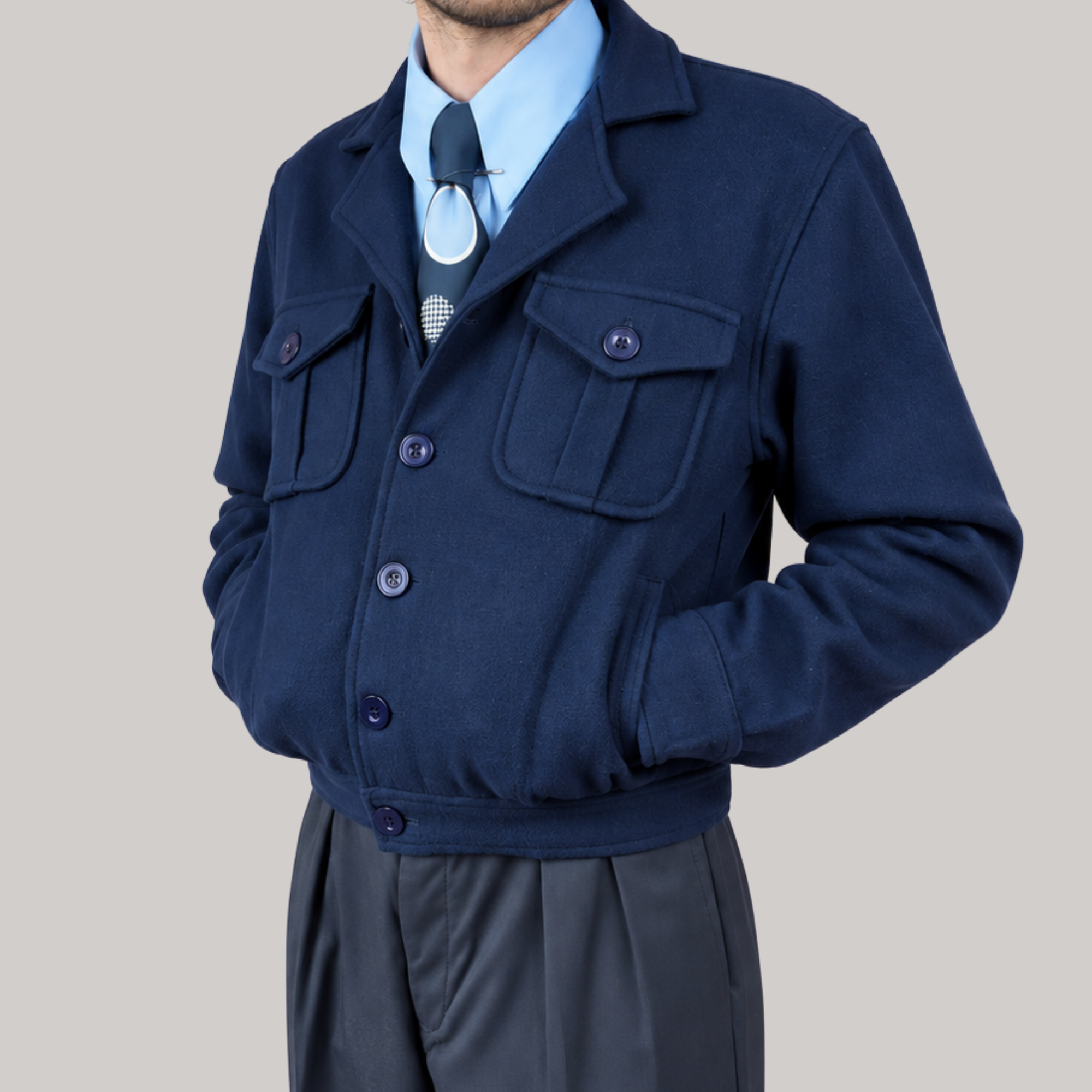 A man wearing a navy blue button-up jacket over a light blue dress shirt and dark tie, paired with dark gray trousers, shown from the neck down against a solid light gray background.