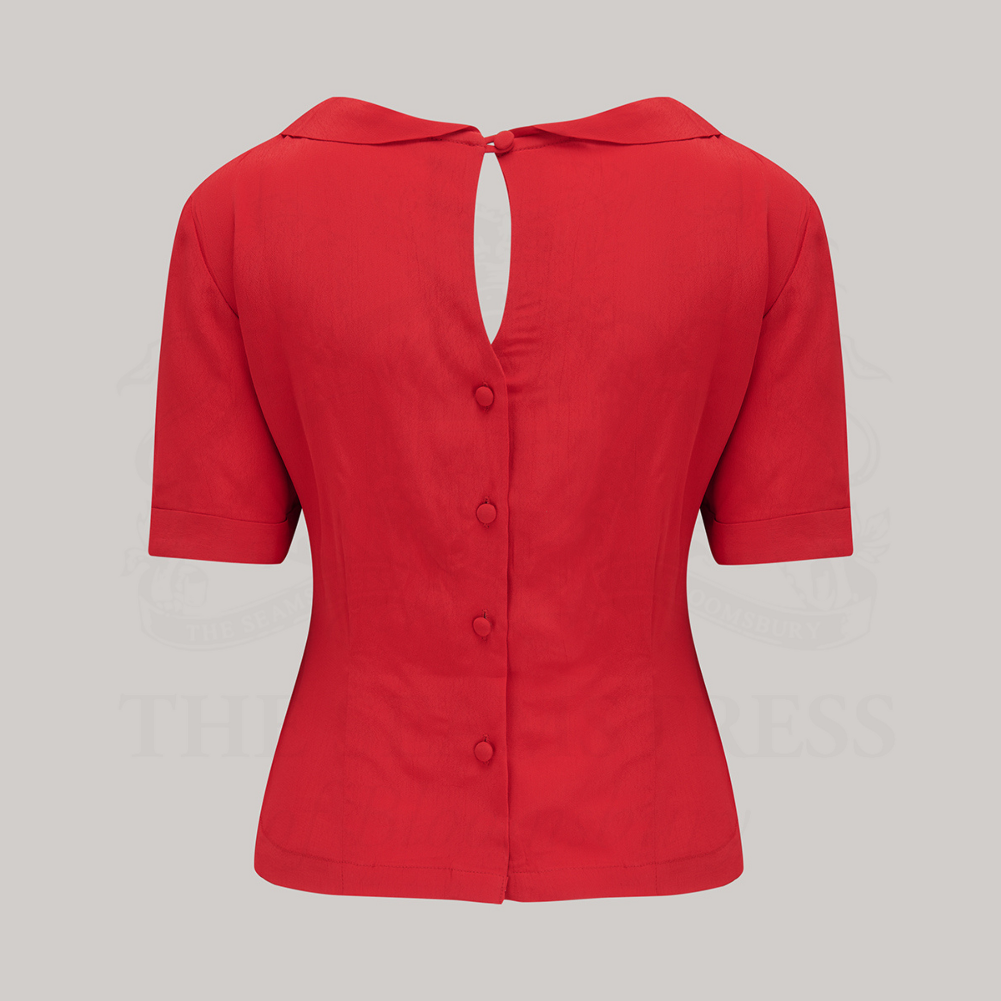 A 1940s style short sleeve red blouse. Featuring a side tie-neck collar and button fastenings down the back of the blouse.
