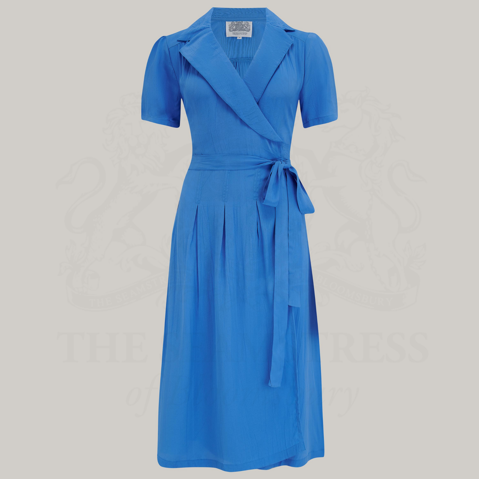 A blue v-neck dress with a tie at the waist, featuring box pleats at the waistband and side-seam pockets.