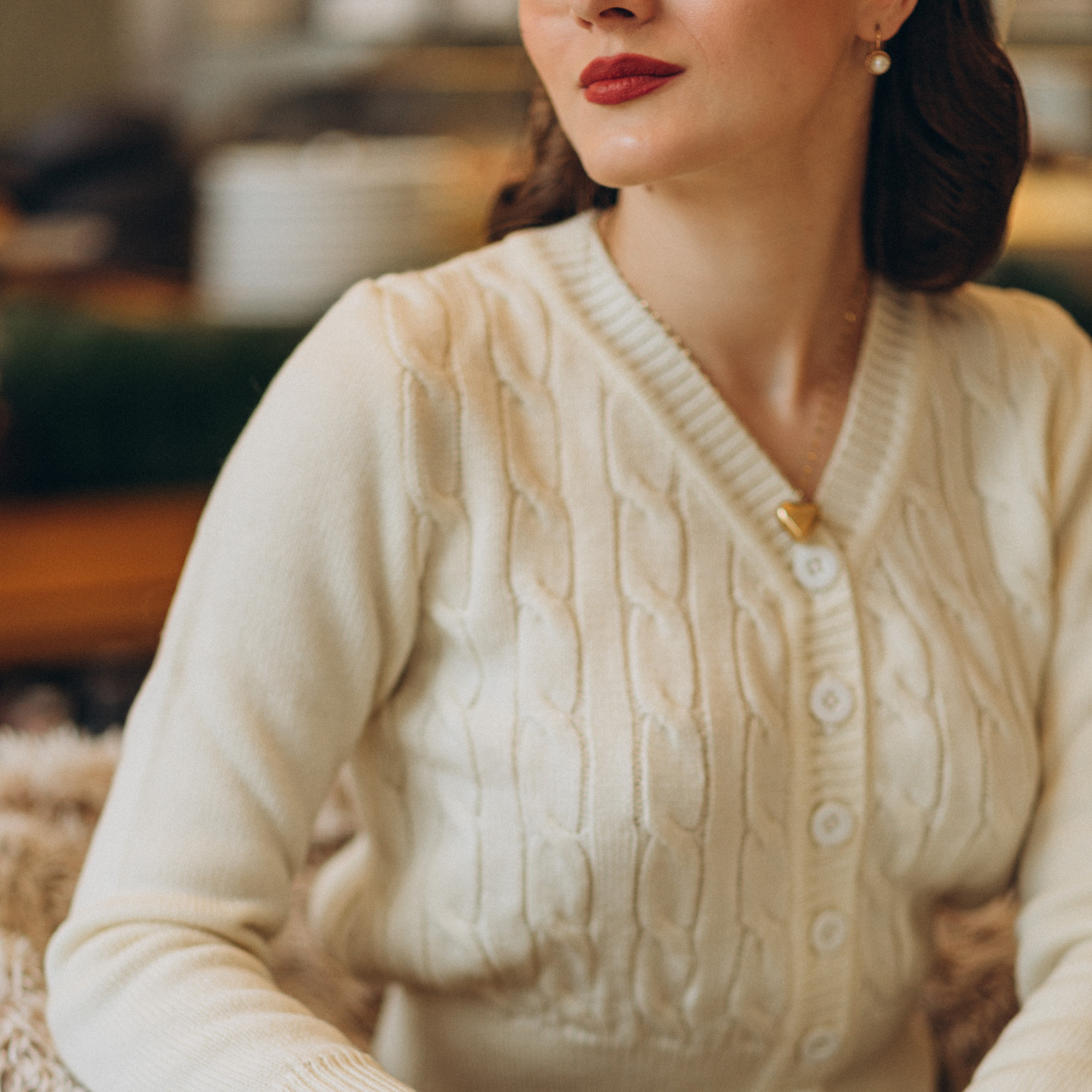 Model wears a 1940s style cable knitted cardigan in cream. Matching cream buttons feature down the front of the cardigan.