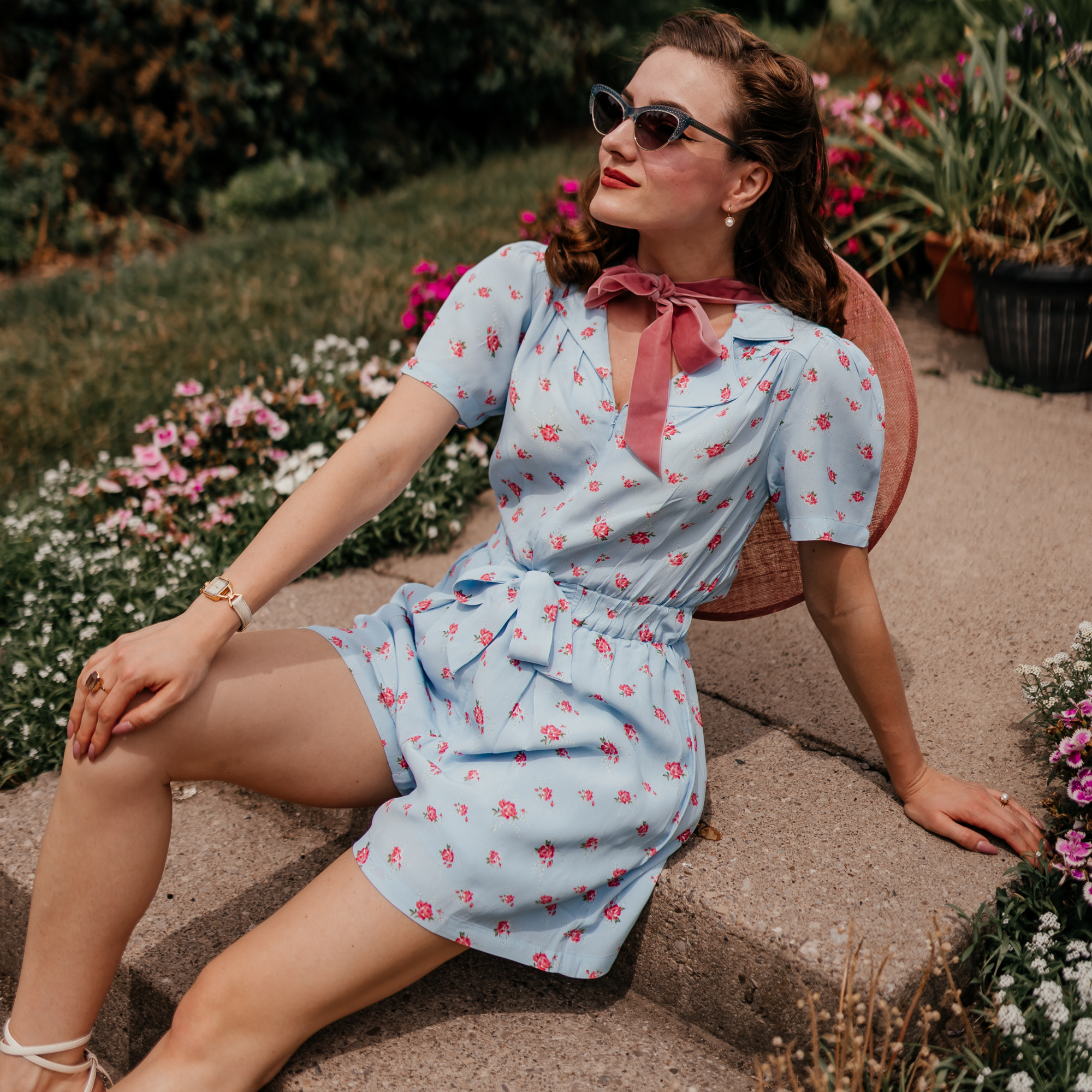 Model wears a 1940s-style playsuit in a powder blue colour with floral design. Playsuit has a zip down the front, short sleeves, and short legs.