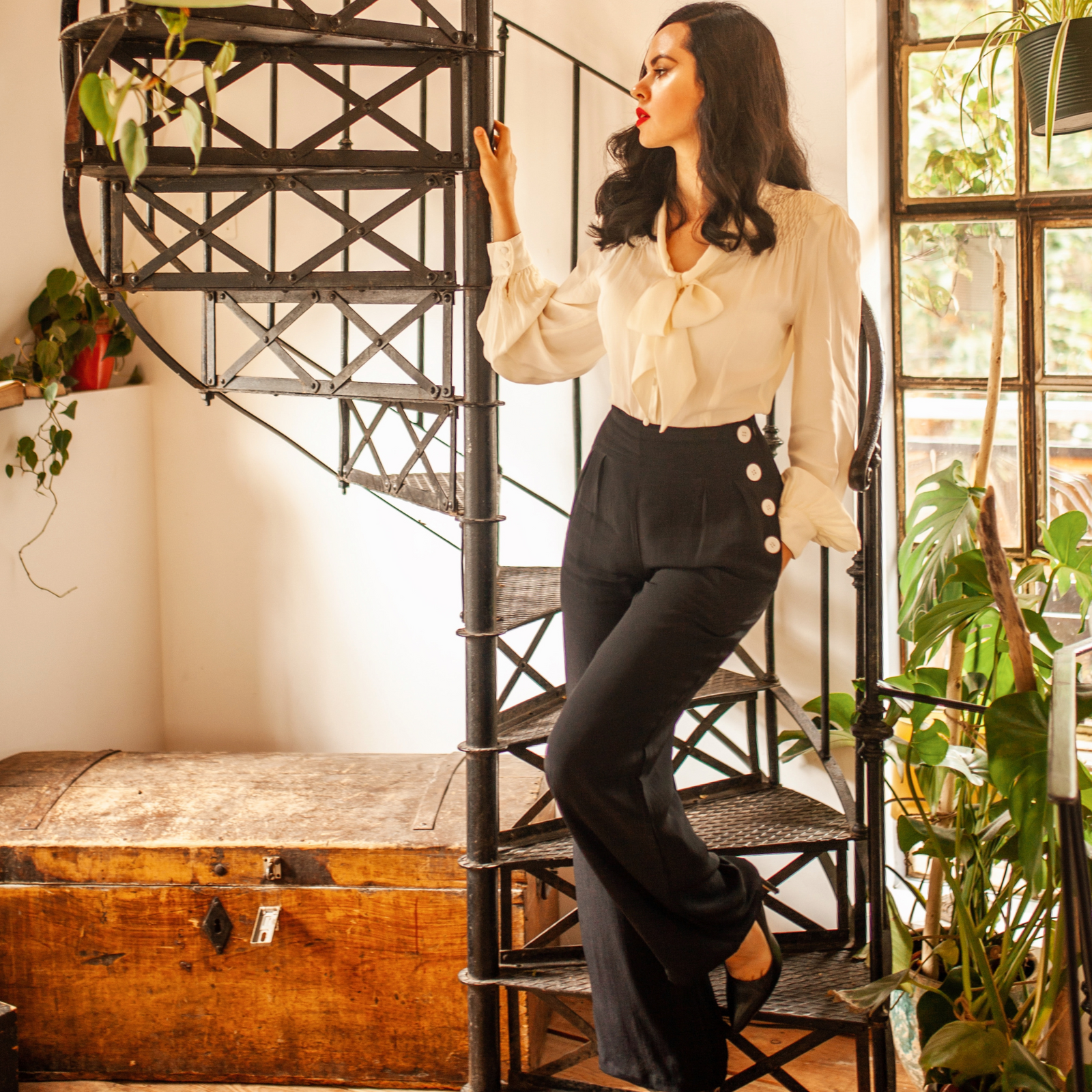 Model wearing 1940s style wide-leg trousers with a long-sleeved cream blouse, stood on stairs