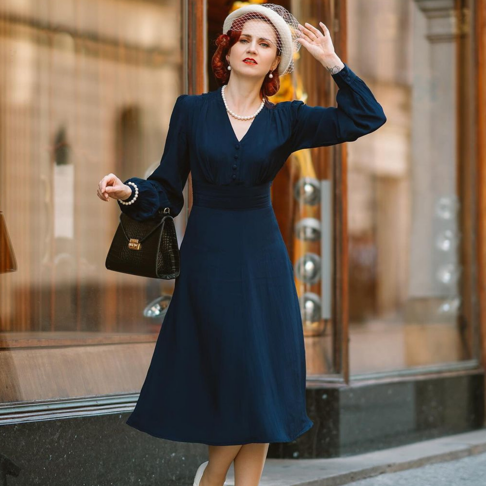 Model wears a 1940s style long sleeve dress in navy. Featuring gauged-in top yoke detailing on the shoulders. 4 small buttons on the bodice, and a tie-waist belt. 
