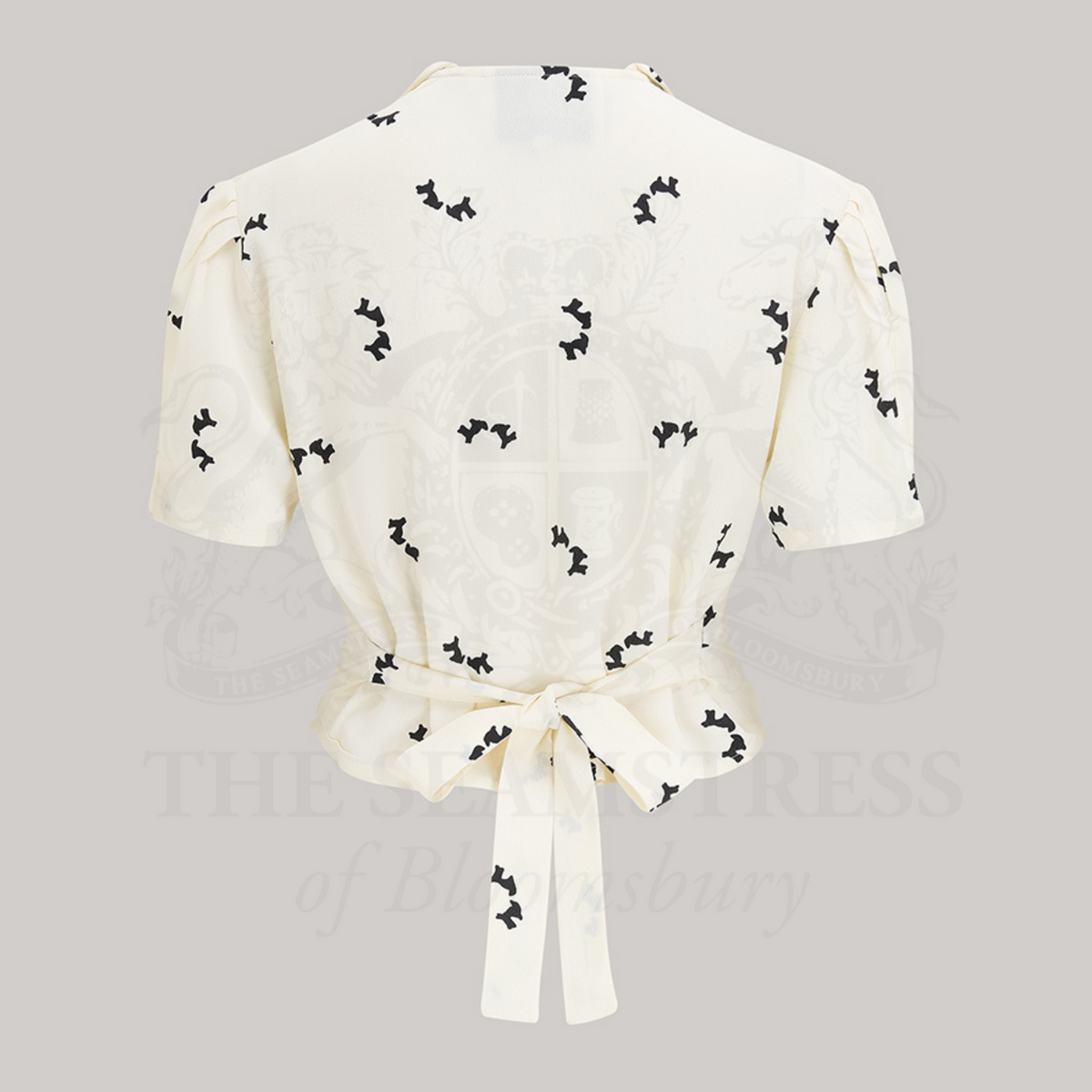 1940s style short sleeve blouse. The blouse is cream coloured with small black dogs dotted around the blouse. Featuring a Peter-Pan front collar, buttons down the front, and a tie-waist belt. 