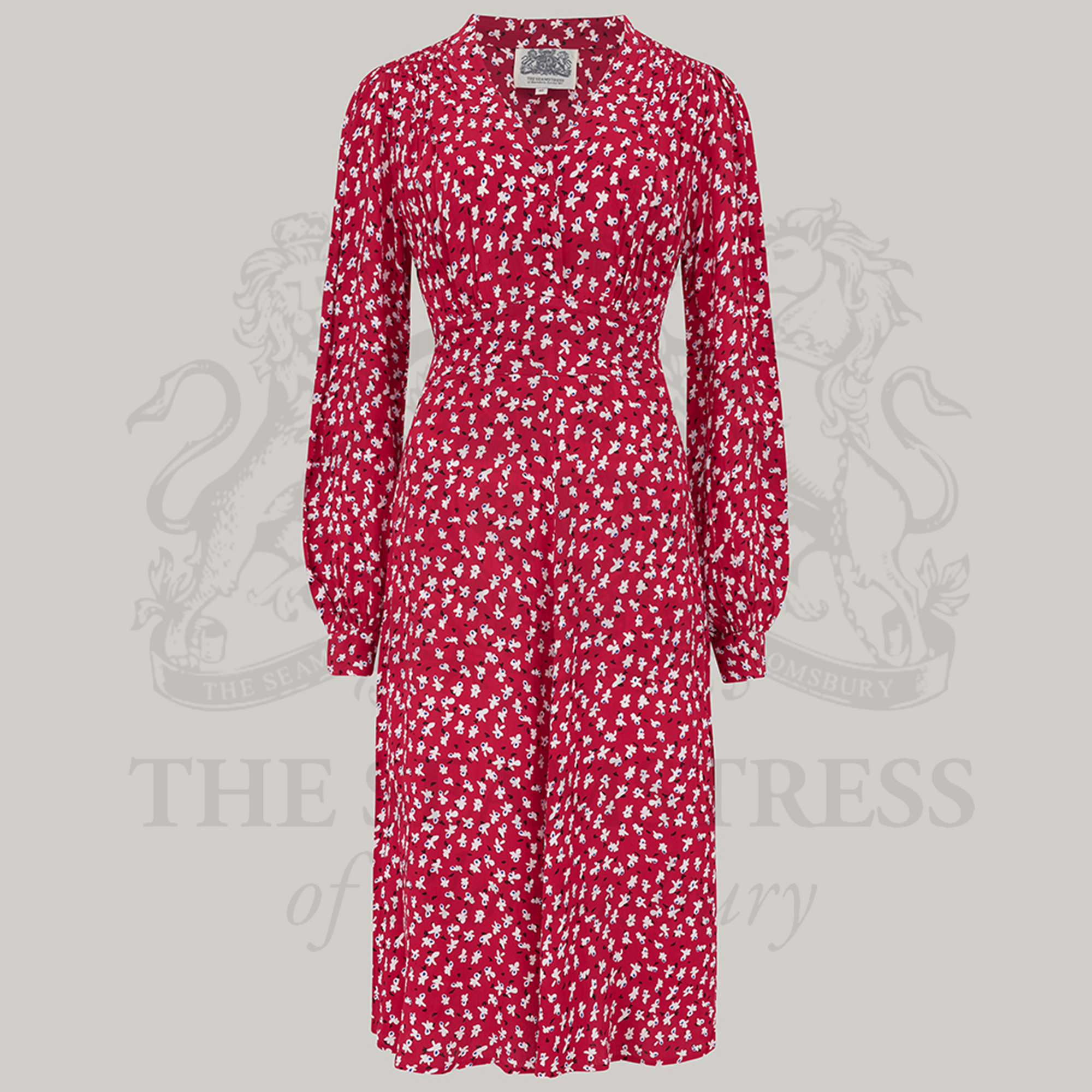 A 1940s style long sleeve dress in red with small clove patterns. Featuring gauged-in top yoke detailing on the shoulders and sleeves that puff out fully at the cuff. 4 small buttons down the front of the dress, and a tie-waist belt. 