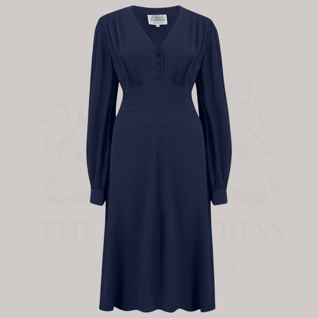 A 1940s-style long-sleeve dress in navy blue. Featuring gauged-in top yoke detailing on the shoulders and sleeves that puff out fully at the cuff. 
