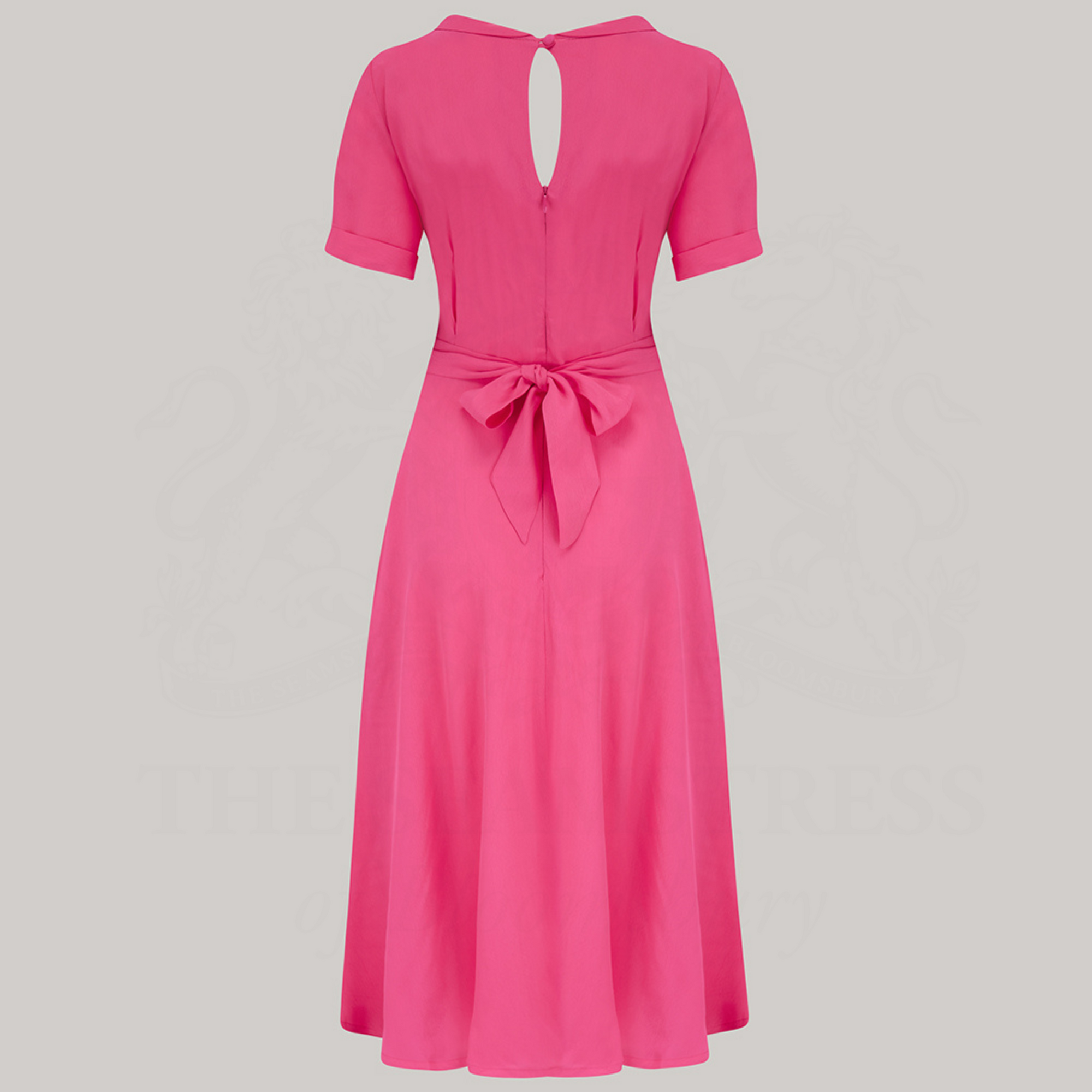 A 1940s-style short-sleeved raspberry pink dress. Featuring a side tie-neck collar and zip fastening back, with a tie-waist belt
