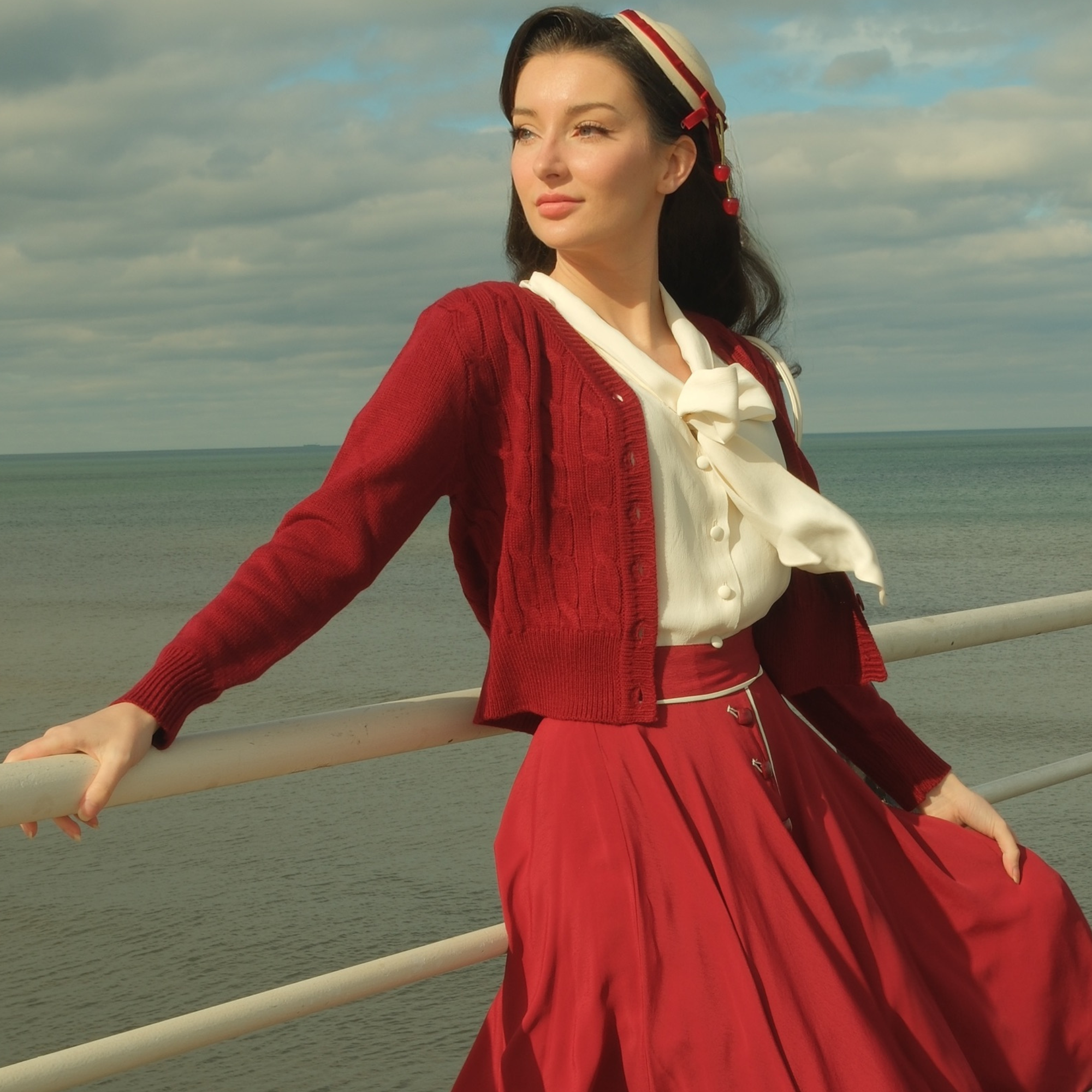 Woman in a red outfit standing by a railing with ocean and sky in the background