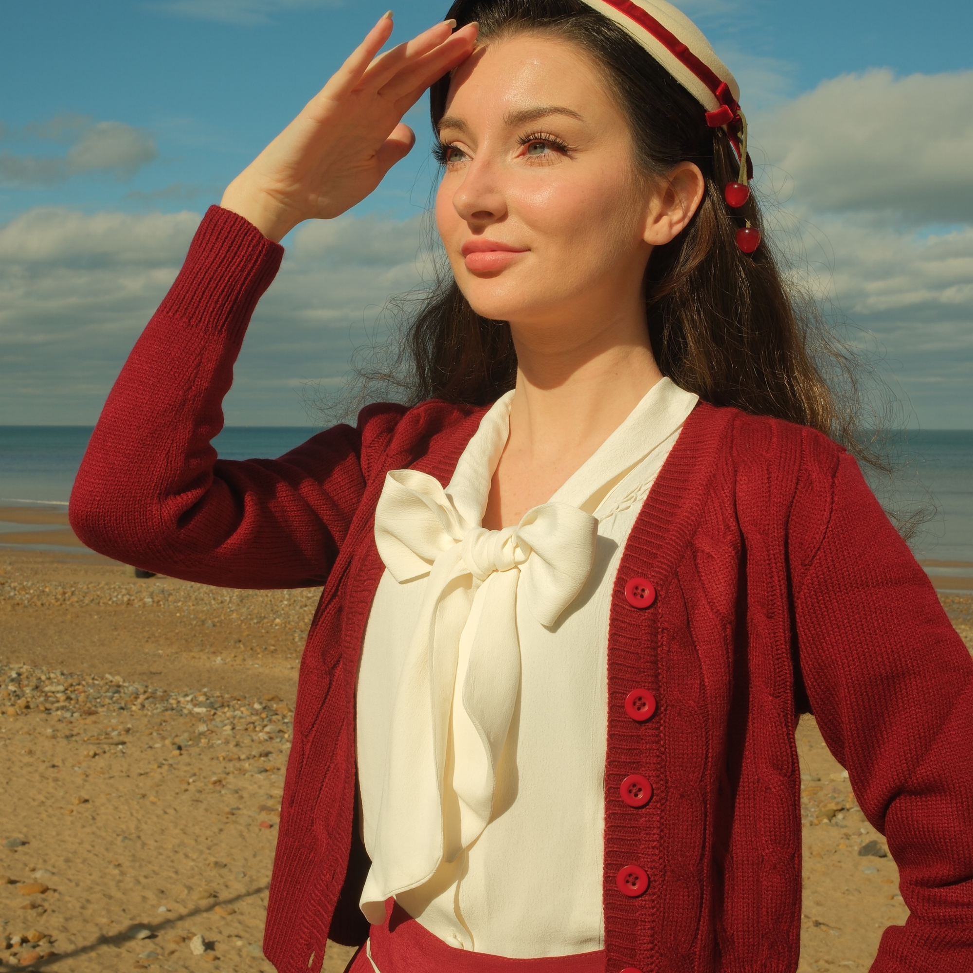 Woman in a wine cardigan and cream blouse on a beach