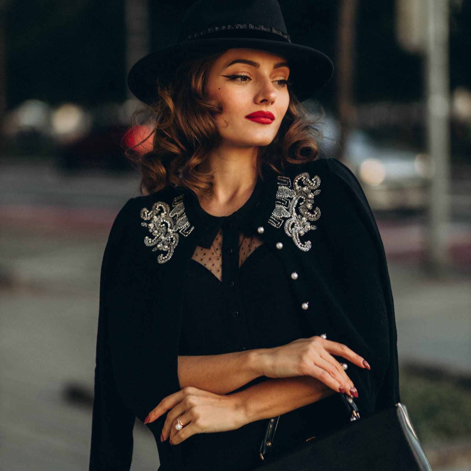 A woman wearing a black hand beaded cardigan with intricate beadwork, paired with a hat and red lipstick.