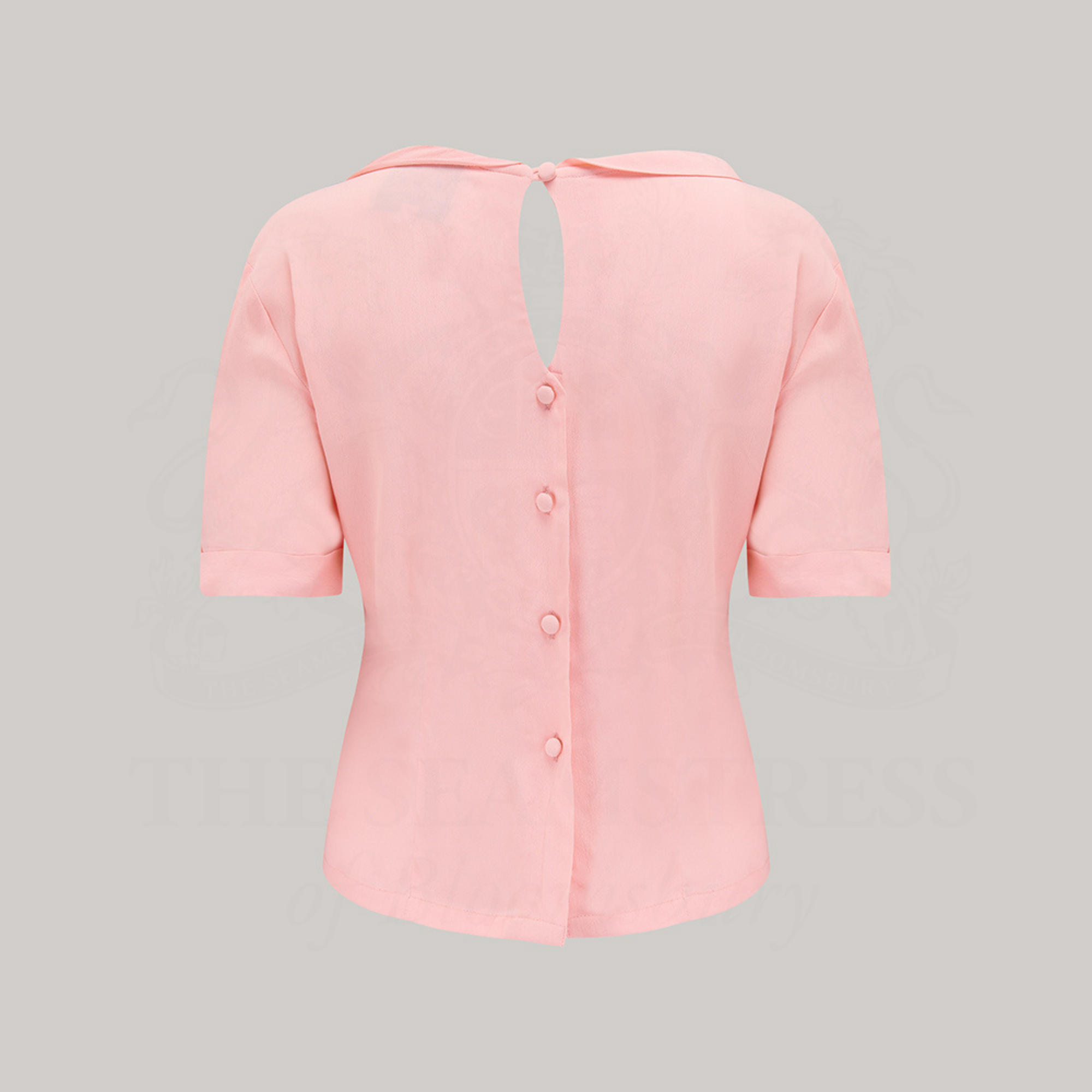 A 1940s style short sleeve pink blouse. Featuring a side tie-neck collar and button fastenings down the back of the blouse.
