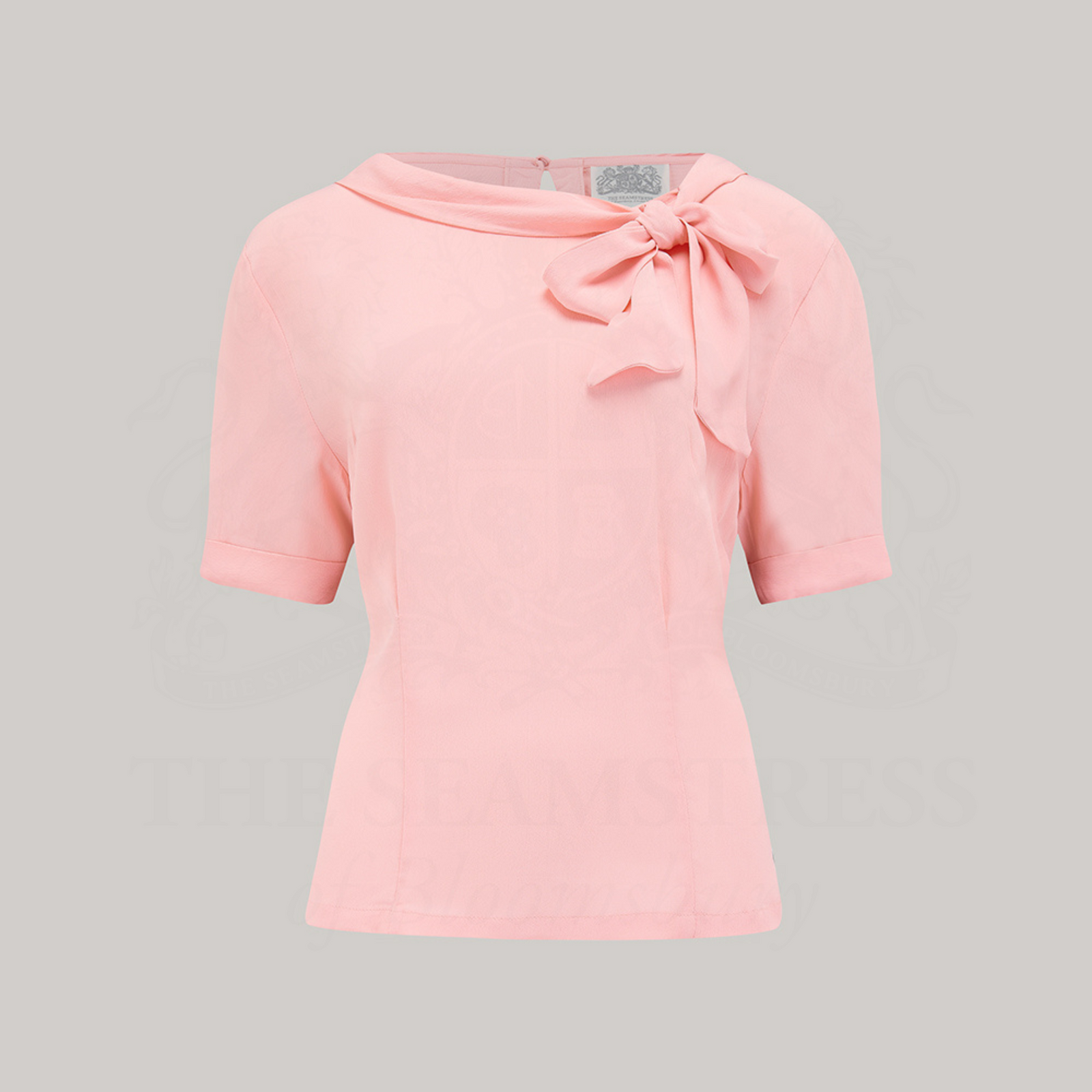 A 1940s style short sleeve pale pink blouse. Featuring a side tie-neck collar and button fastenings down the back of the blouse.
