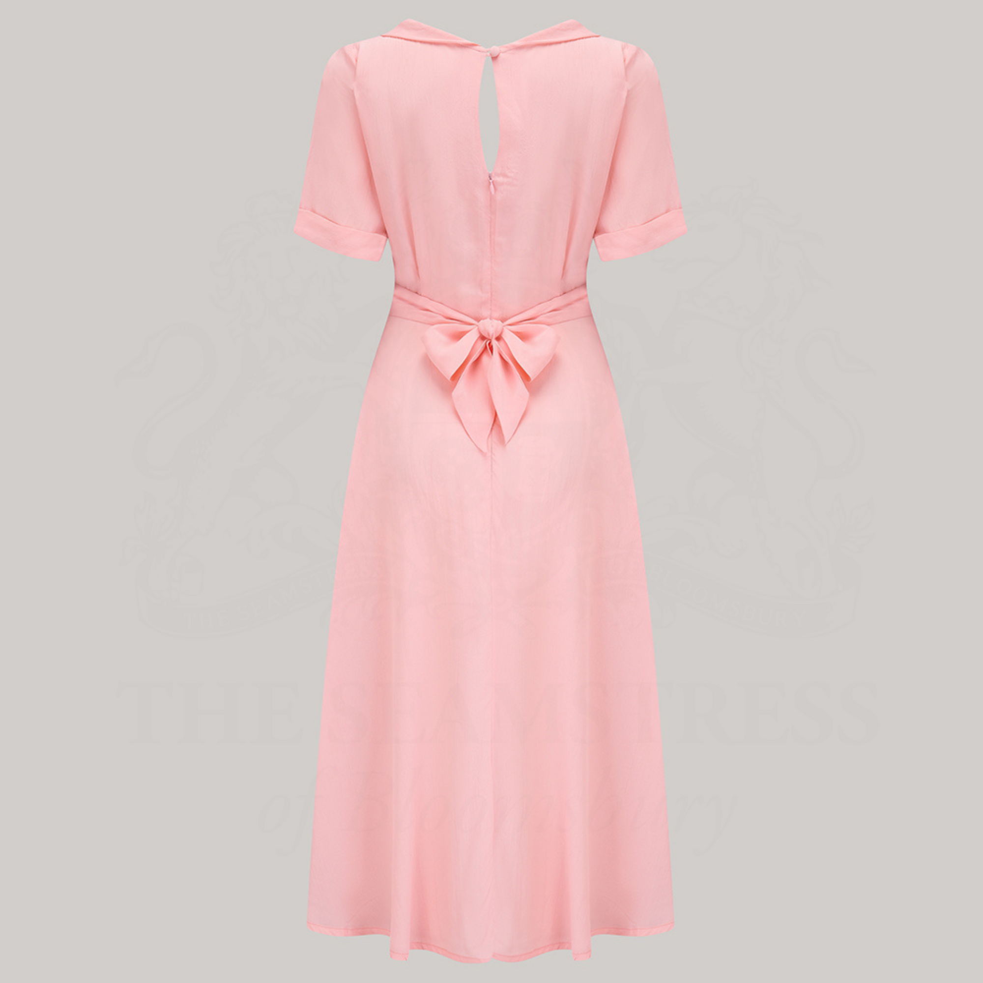 A 1940s-style short-sleeved pale pink dress. Featuring a side tie-neck collar and zip fastening back, with a tie-waist belt
