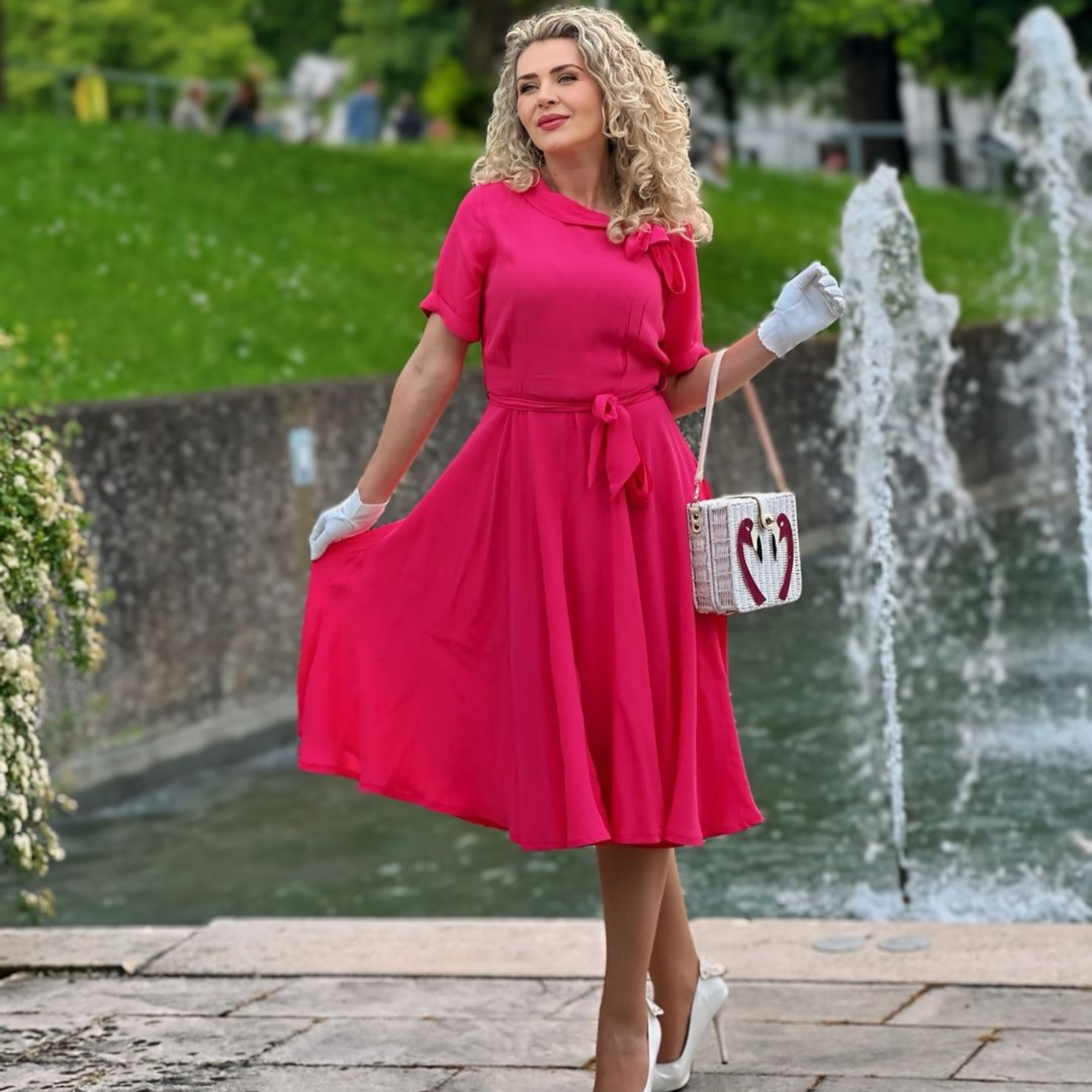 Model wears a raspberry pink short-sleeved 1940s-style dress with a side bow collar and adjustable tie-waist belt