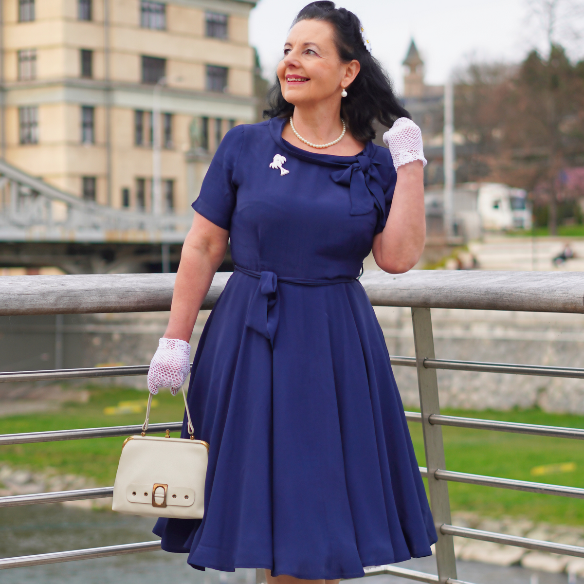 Model wears a navy blue short-sleeved 1940s-style dress with a side bow collar and adjustable tie-waist belt