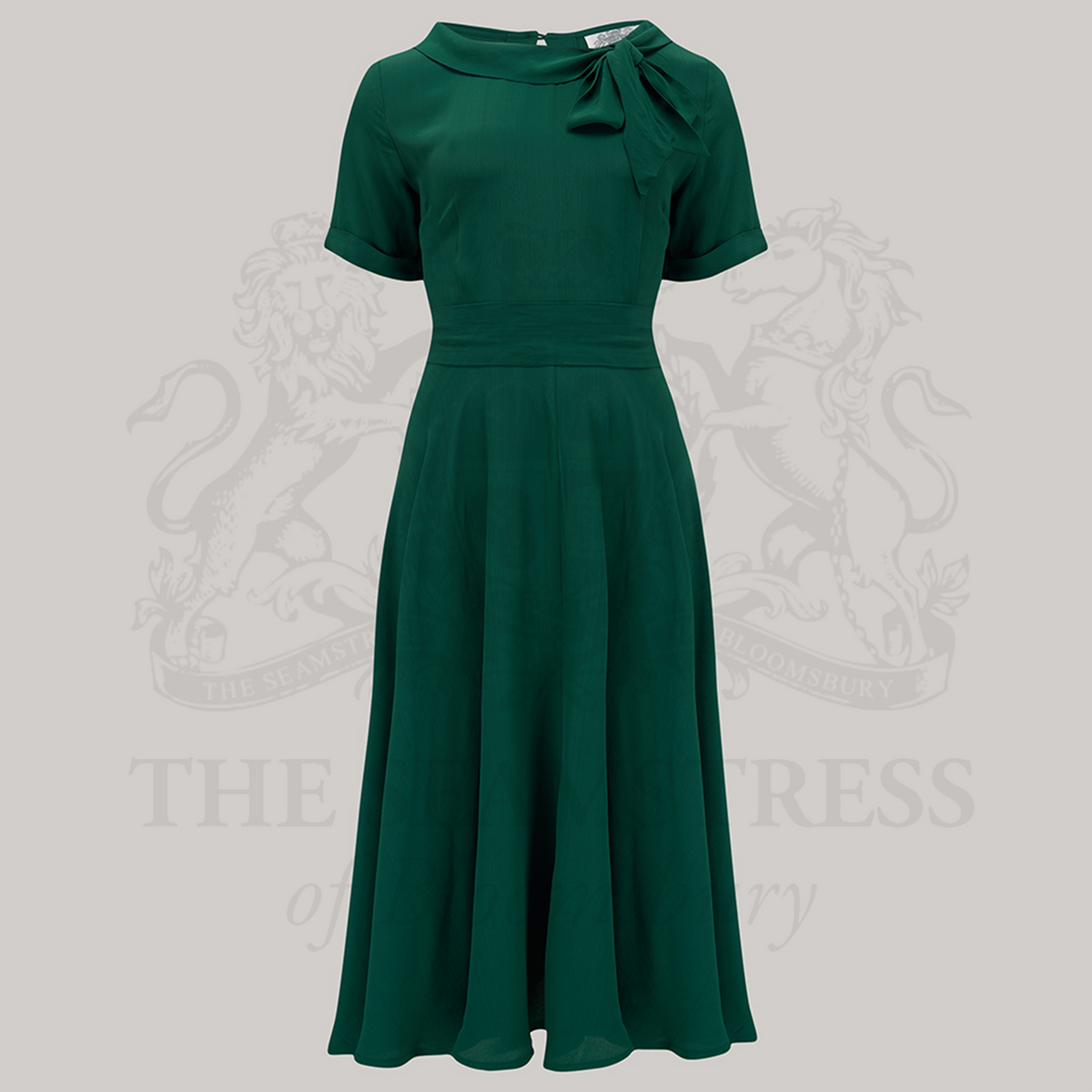 A 1940s vintage style short sleeve dress with a side tie-neck and a tie-waist belt. This dress is in a dark green colour and has a a-line skirt and is designed to finish below the knee.