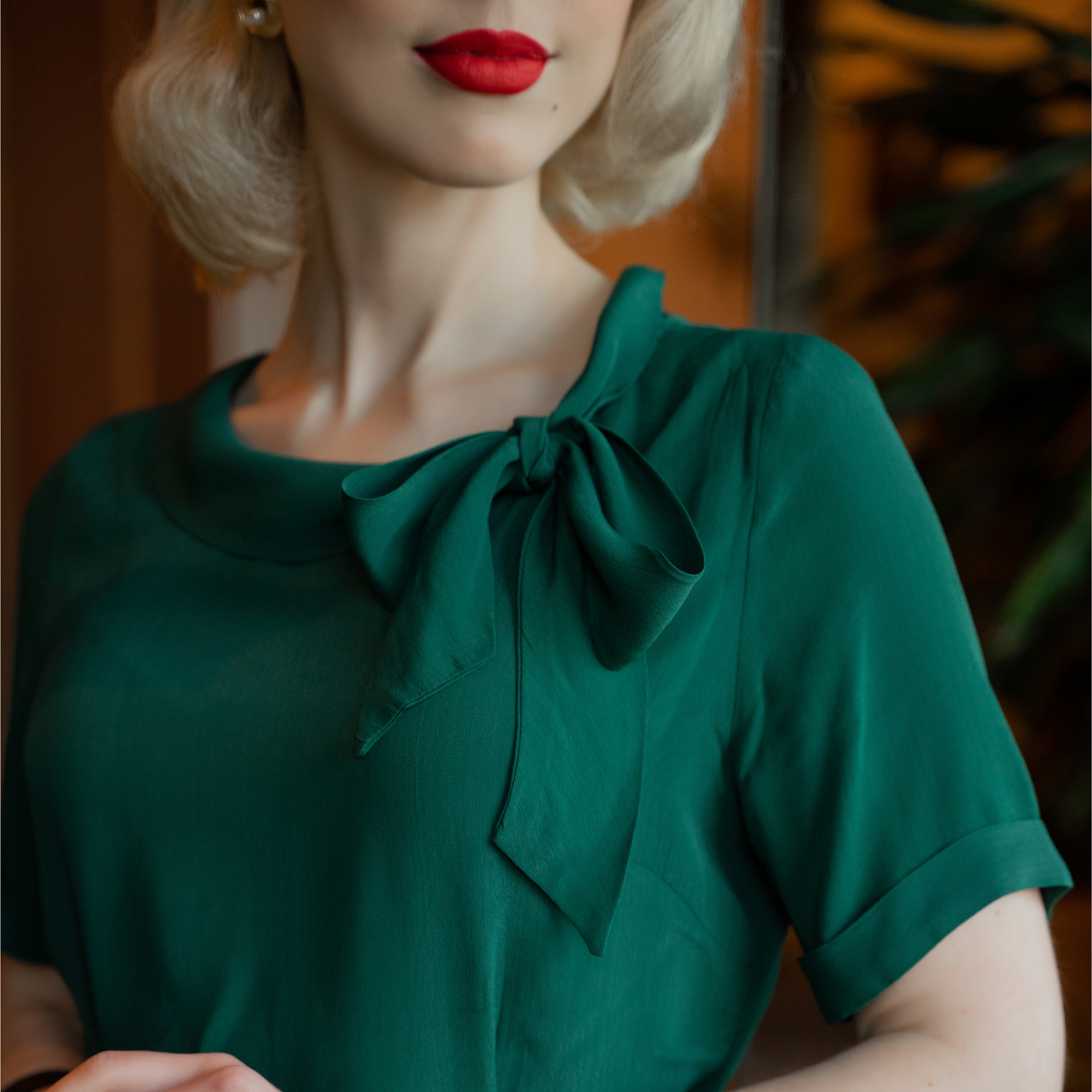 A close up of the collar of a green dress, showing the bow detailing.