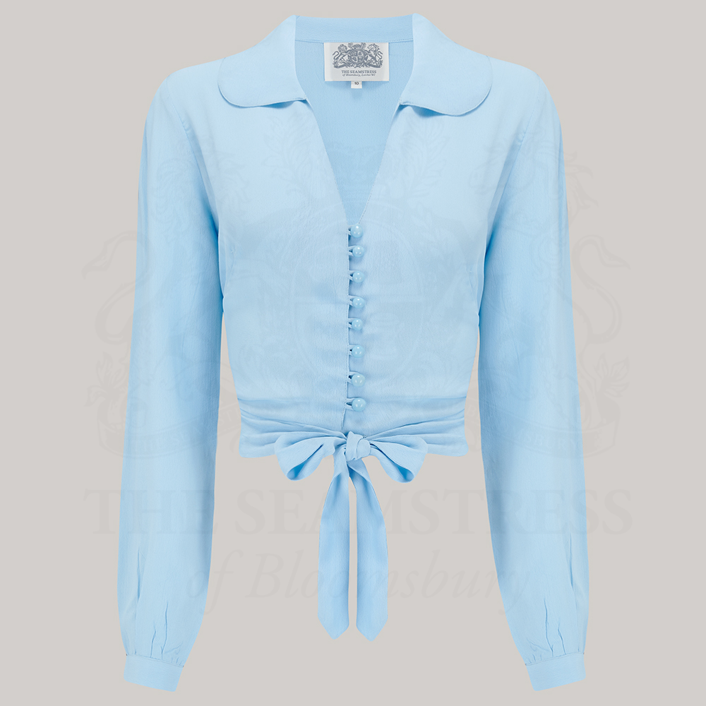 A 1940s-style long-sleeve blouse in pale blue. The blouse has a v-neck, button fastenings on the front, and a waist tie.
