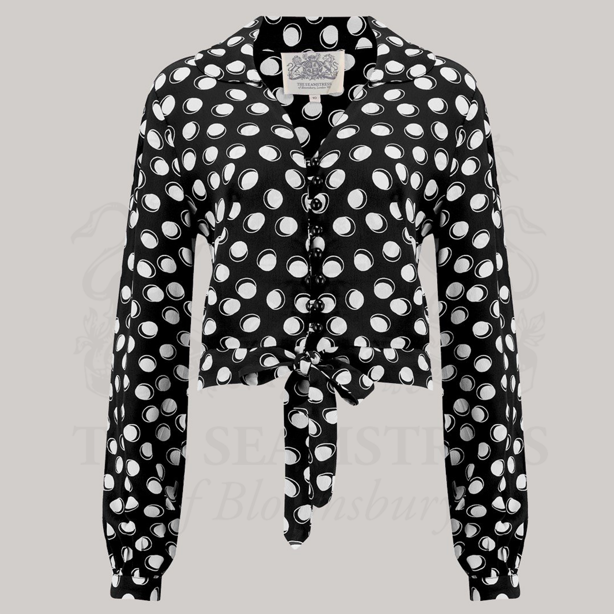 A black blouse with white polka dots, featuring a round collar, long sleeves, button closures, and a tie-waist belt.