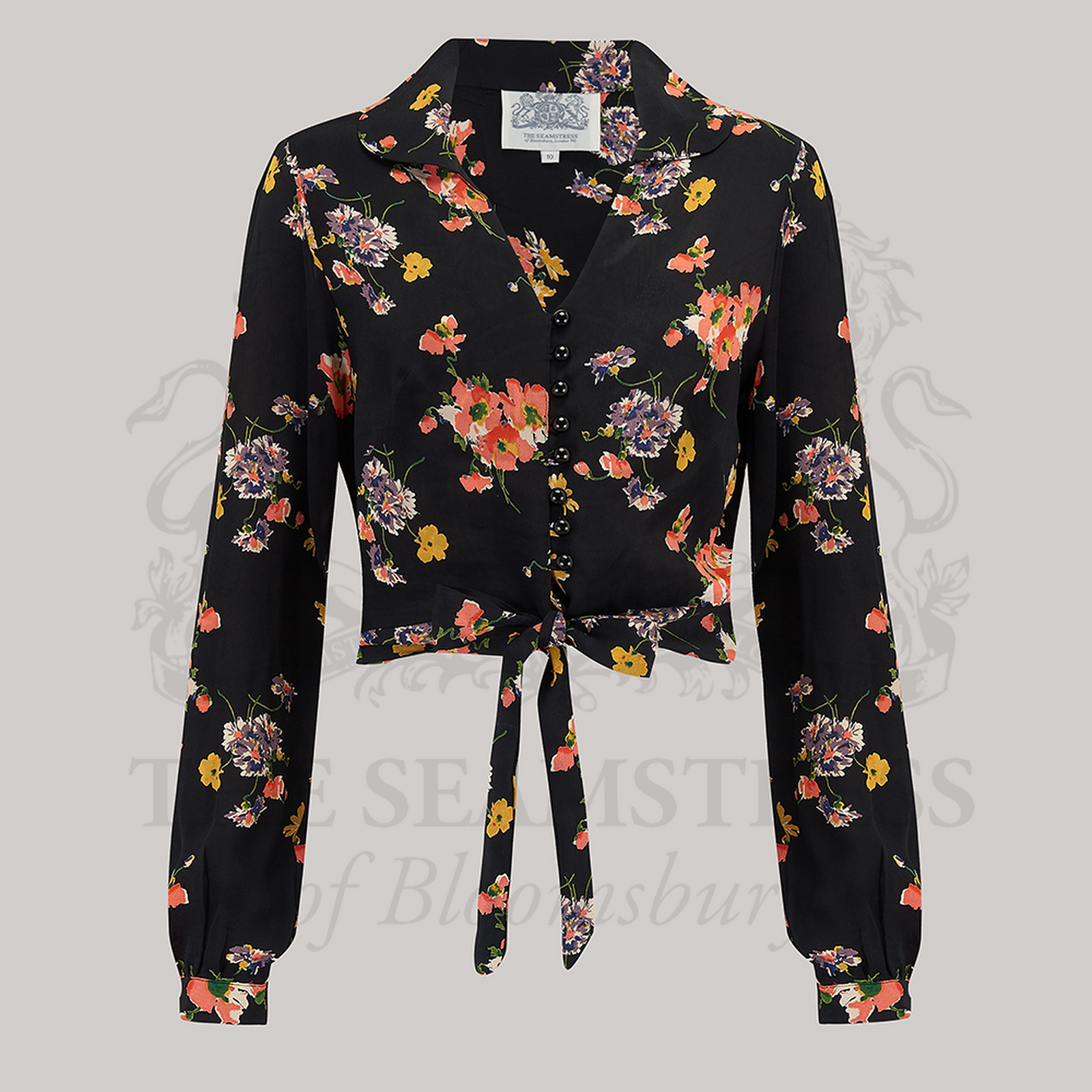 A 1940s-style long-sleeve blouse in black with a floral pattern. The blouse has a v-neck, button fastenings on the front, and a waist tie.
