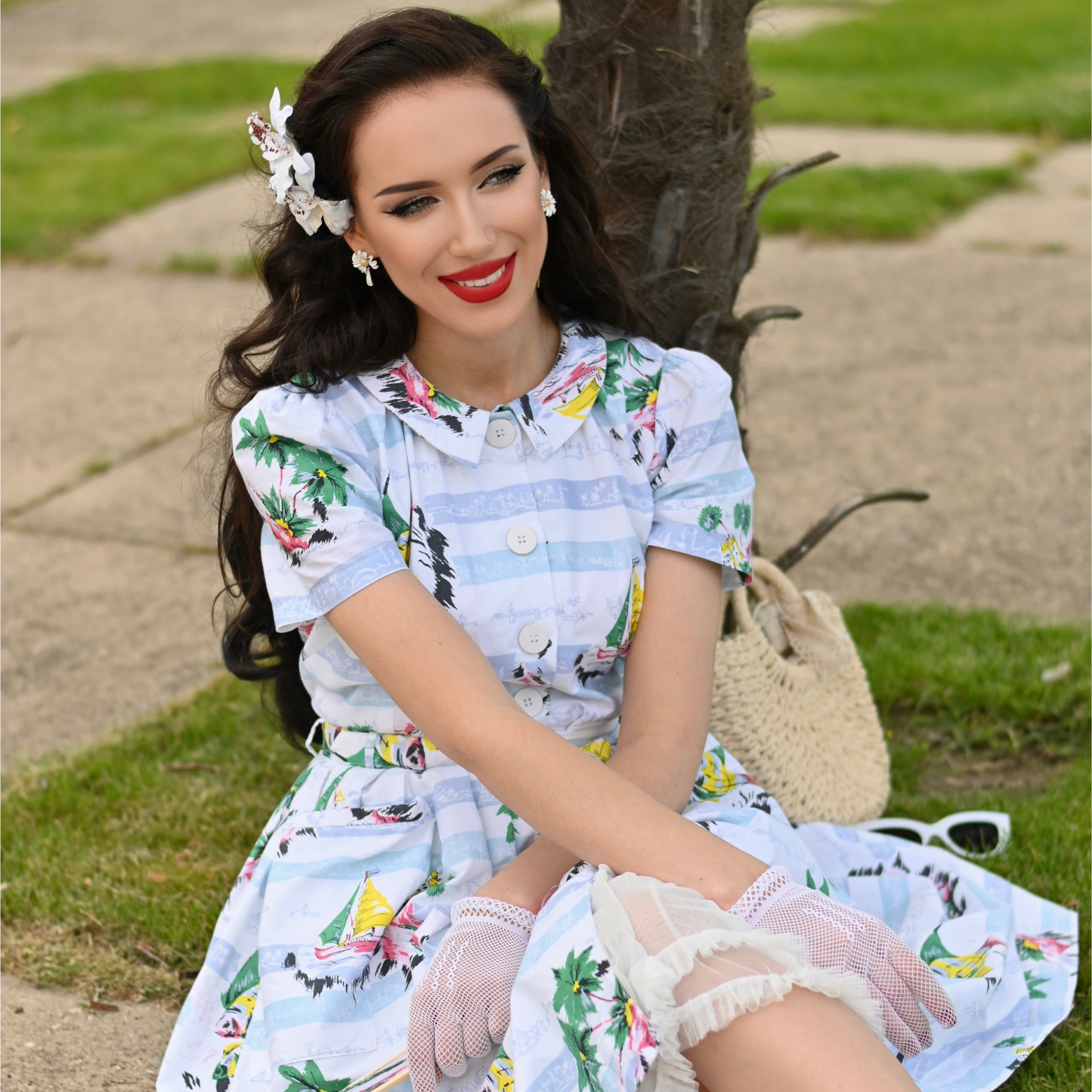 Woman in a floral dress sitting outdoors with a tree and grass in the background