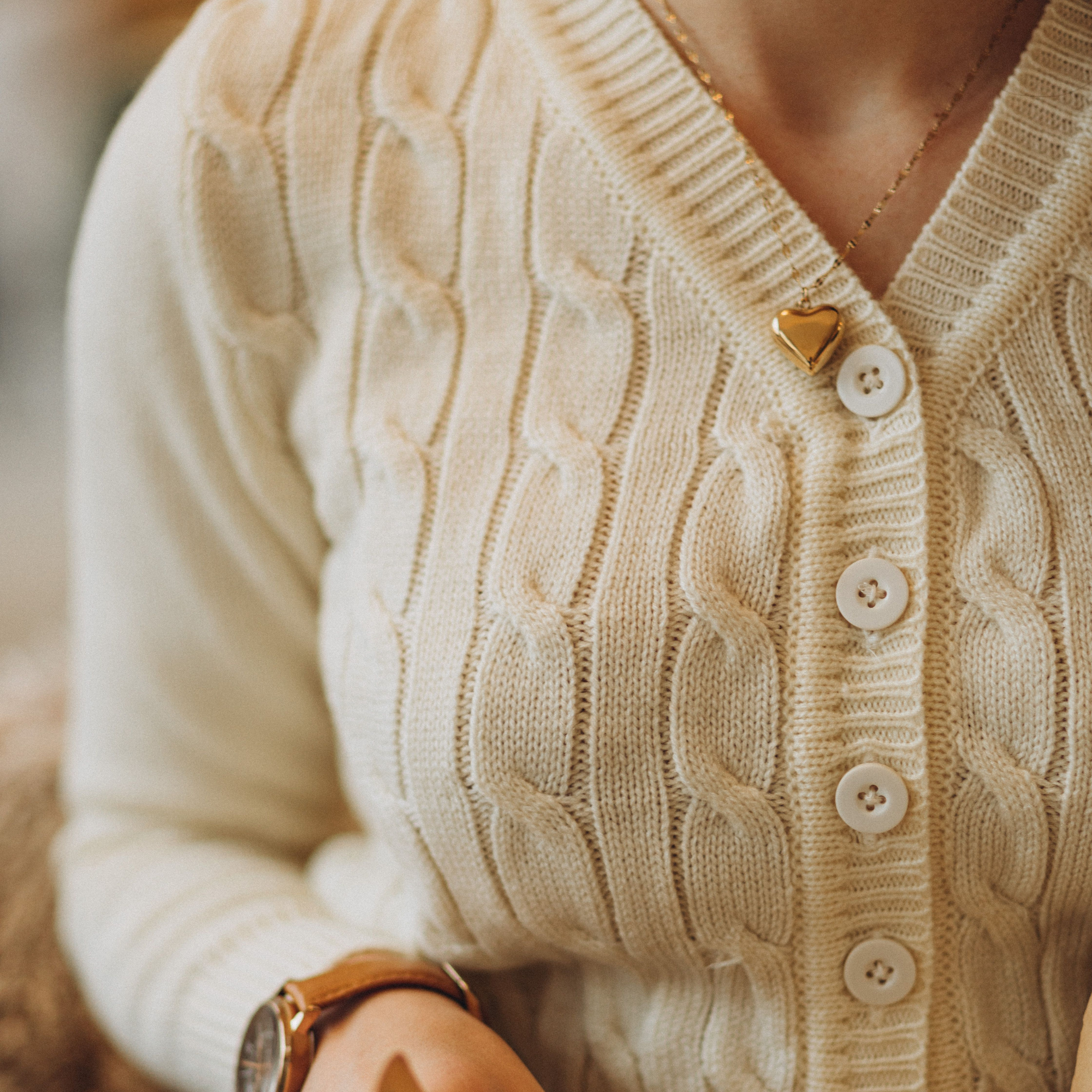 Model wears a 1940s style cable knitted cardigan in cream. Matching cream buttons feature down the front of the cardigan.