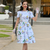 Model wears a 1940s-style short-sleeve dress in a vintage seaside-inspired print. Made from cotton with two front patch pockets, nine buttons down the front of the dress and a matching waist belt.