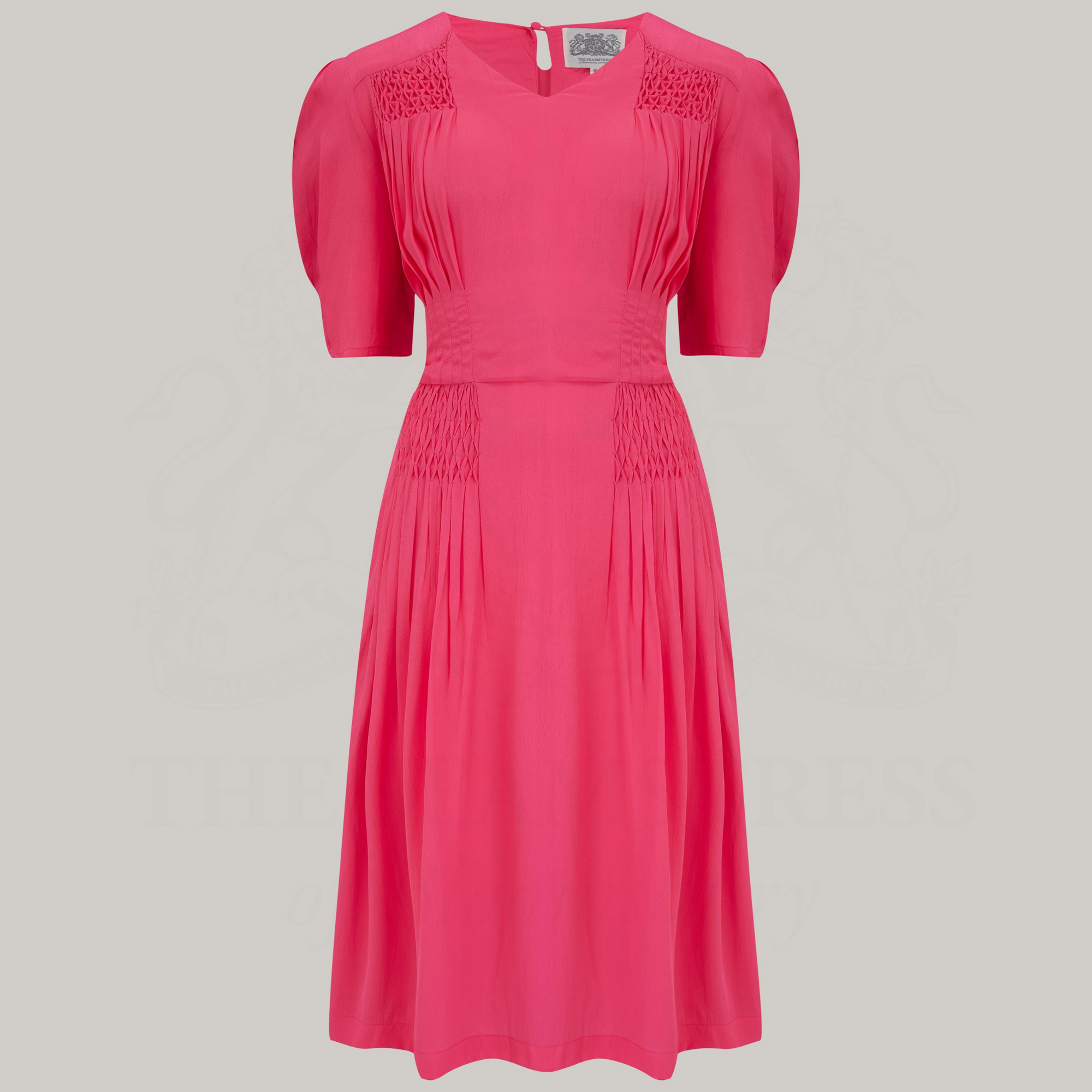 A 1940s-style short-sleeve dress in raspberry pink. Featuring a sweetheart neckline, smocking detailing, pockets, and a waist tie.
