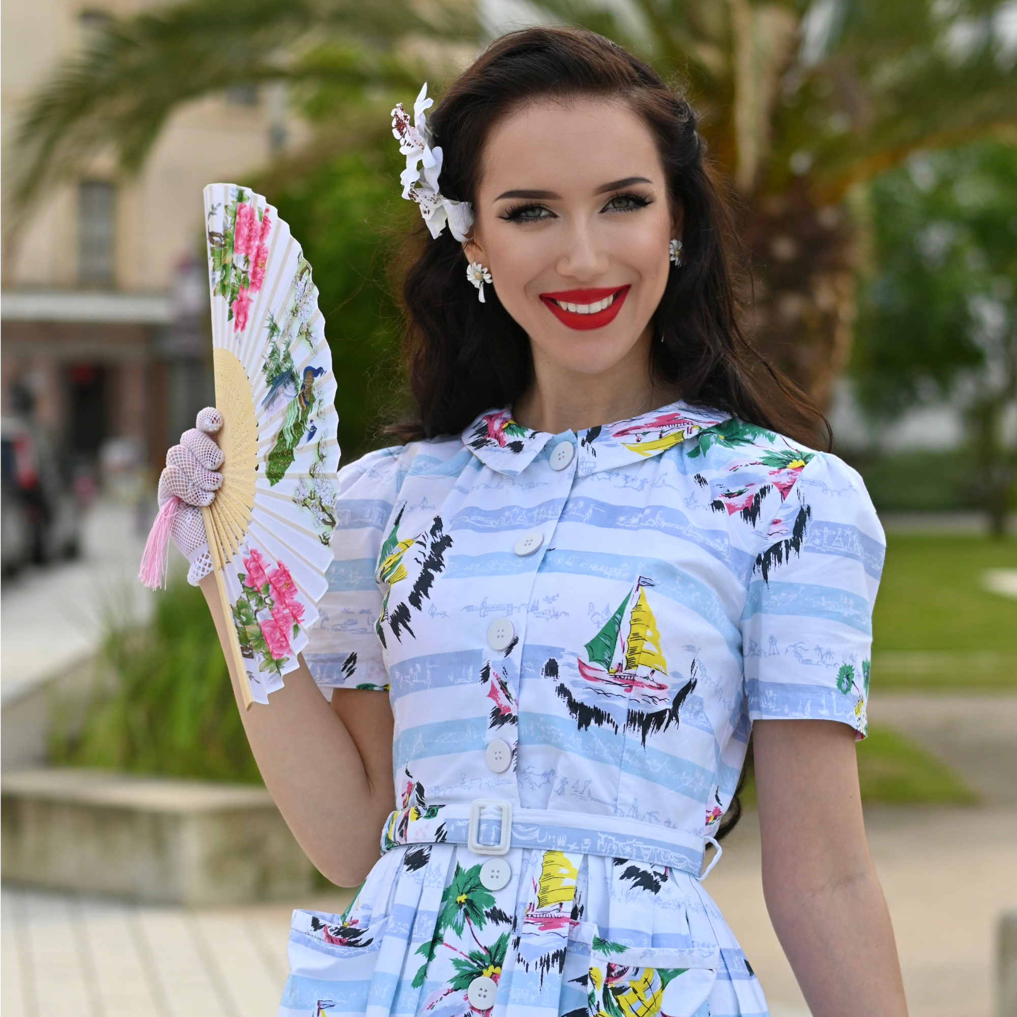 Woman in a colorful dress holding a floral fan outdoors