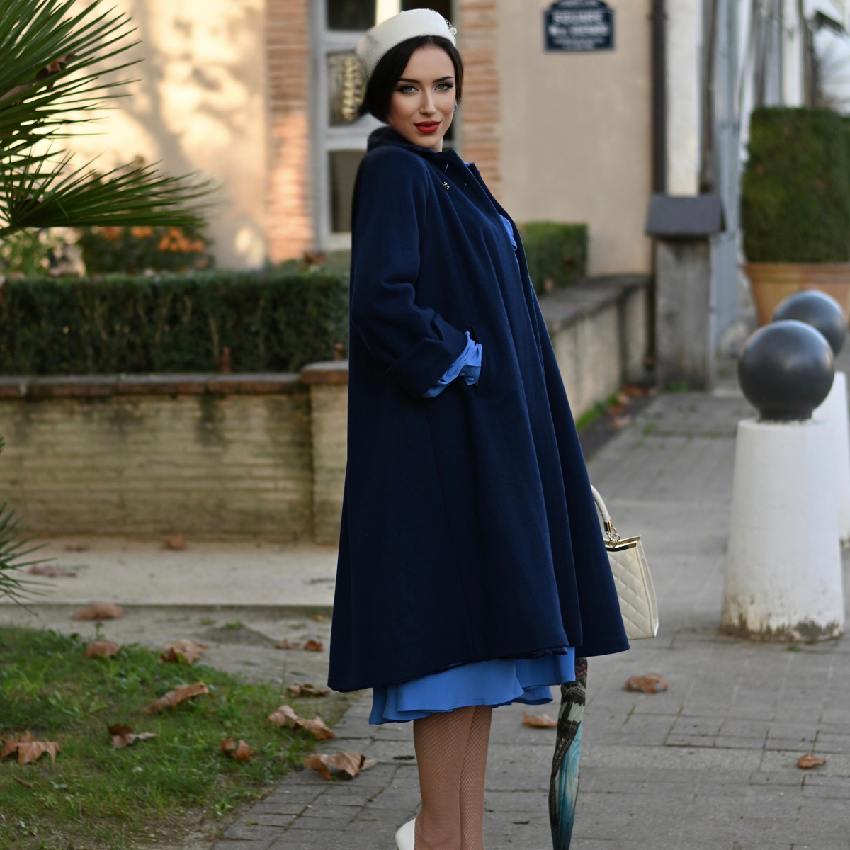 model wears a 1940s style long coat in navy on top of her light blue dress