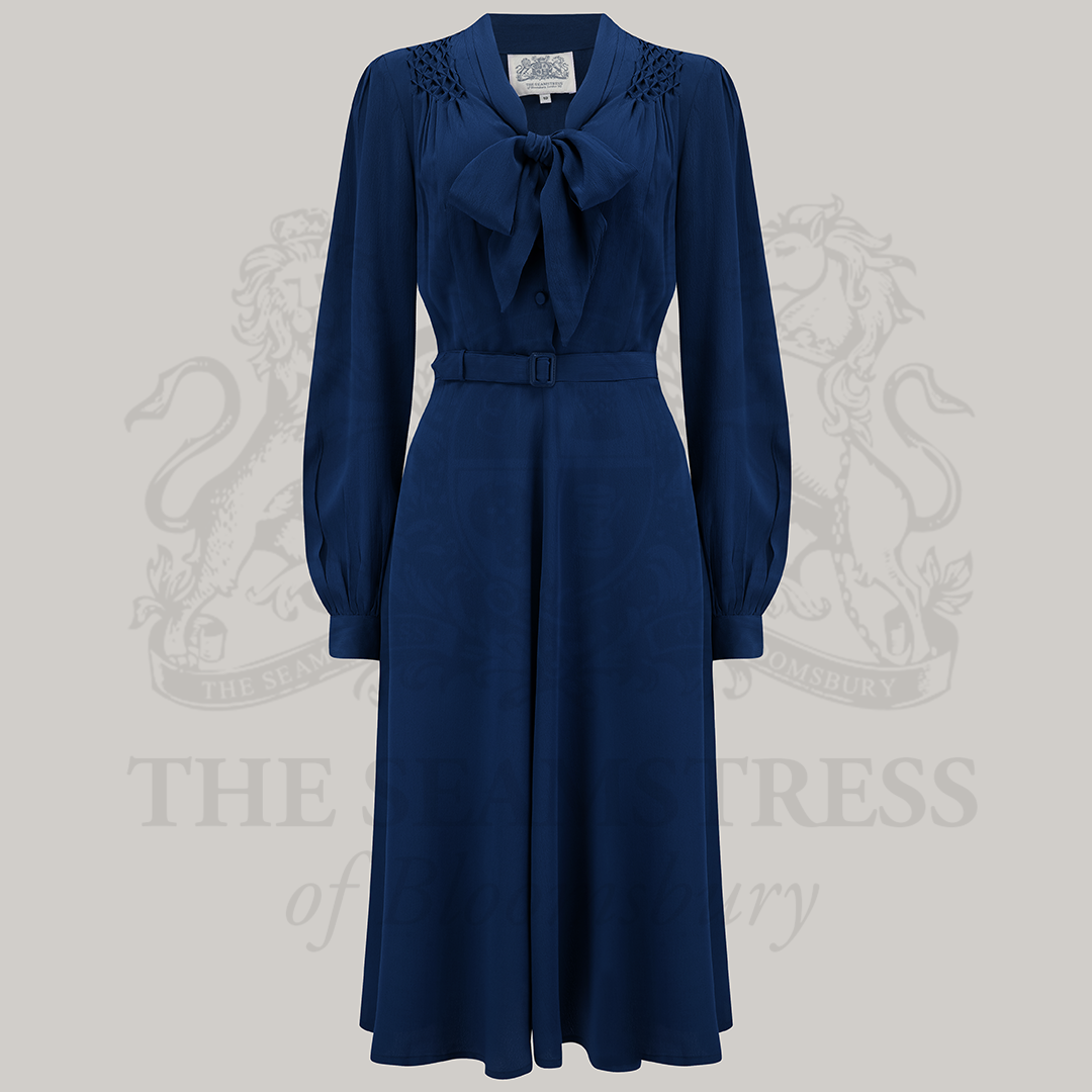 A vintage-inspired navy blue dress with a pussy-bow neckline, long sleeves, and a waist belt