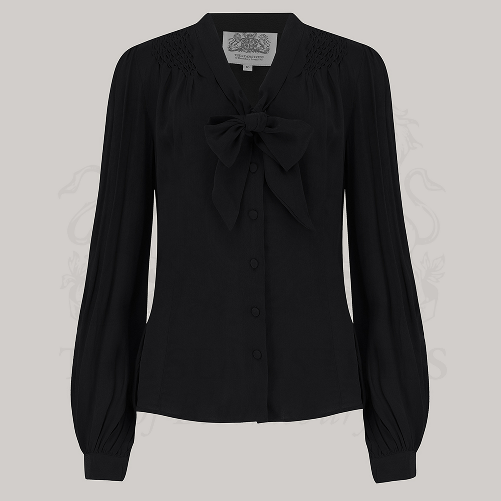 A vintage-inspired black blouse with a pussy-bow neckline, long bishop sleeves with full cuffs, and smock stitching on shoulders, button fastenings, made from Crepe de Chine fabric.
