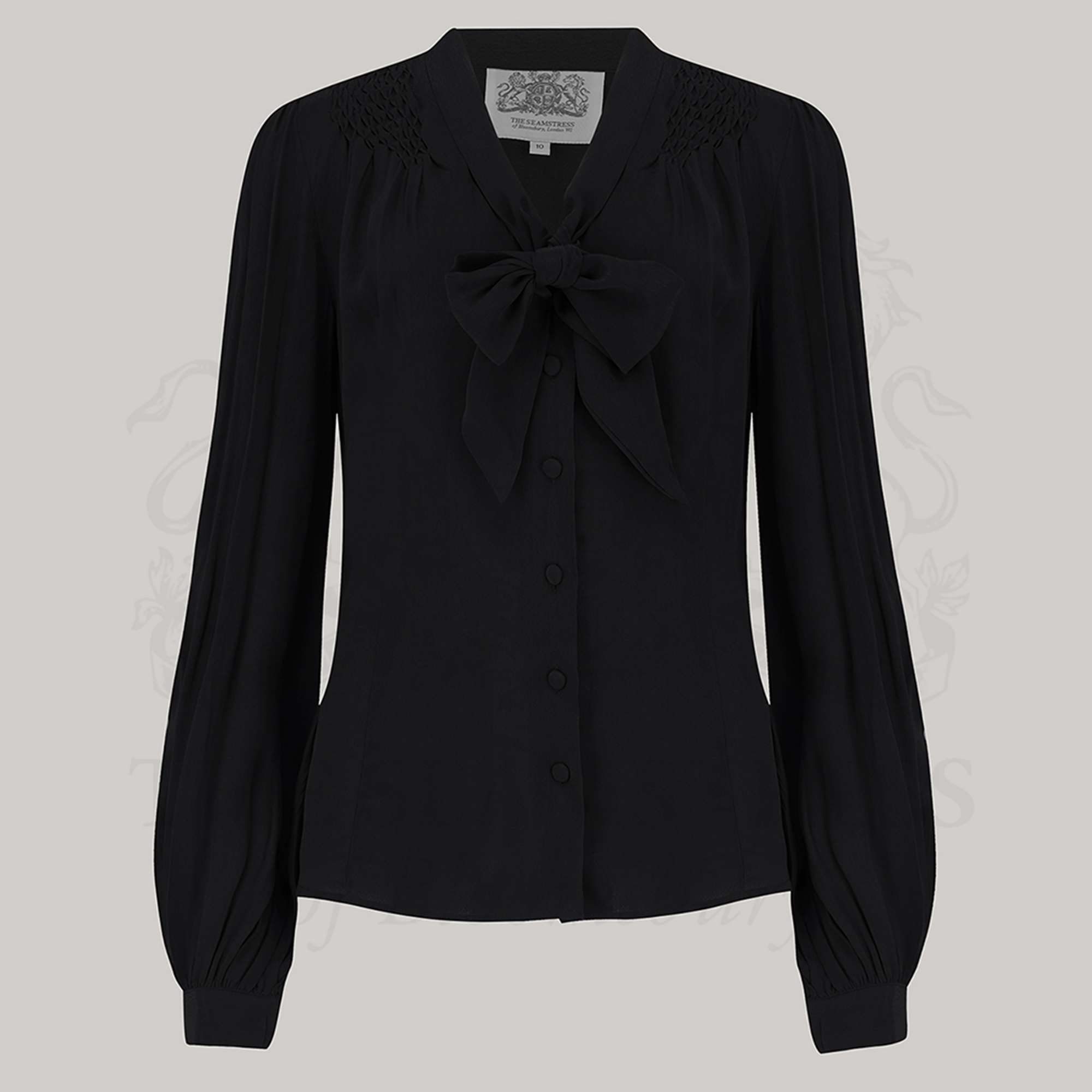 A vintage-inspired black blouse with a pussy-bow neckline, long bishop sleeves with full cuffs, and smock stitching on shoulders, button fastenings, made from Crepe de Chine fabric.