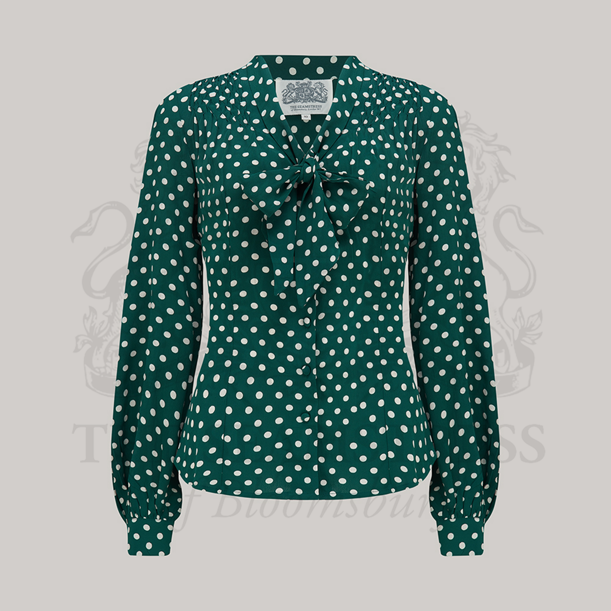 A vintage-inspired green polka dot blouse with a pussy-bow neckline, long bishop sleeves with full cuffs, and smock stitching on shoulders.