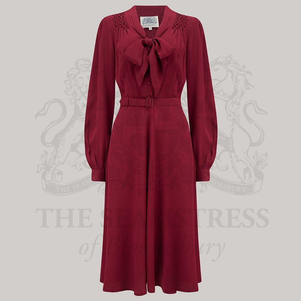 A wine Eva pussy-bow neckline dress with long sleeves and a full cuff, paired with a waist belt and side-seam pockets.