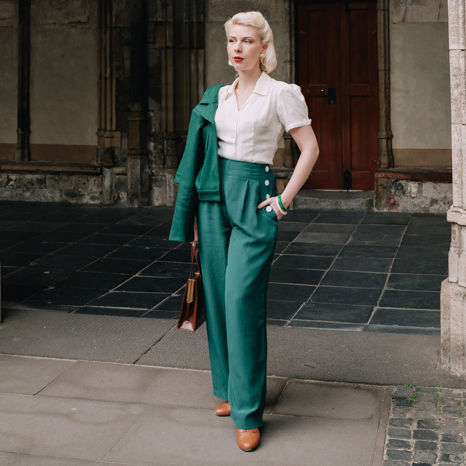 Woman in vintage attire standing on a stone pavement with a building in the background