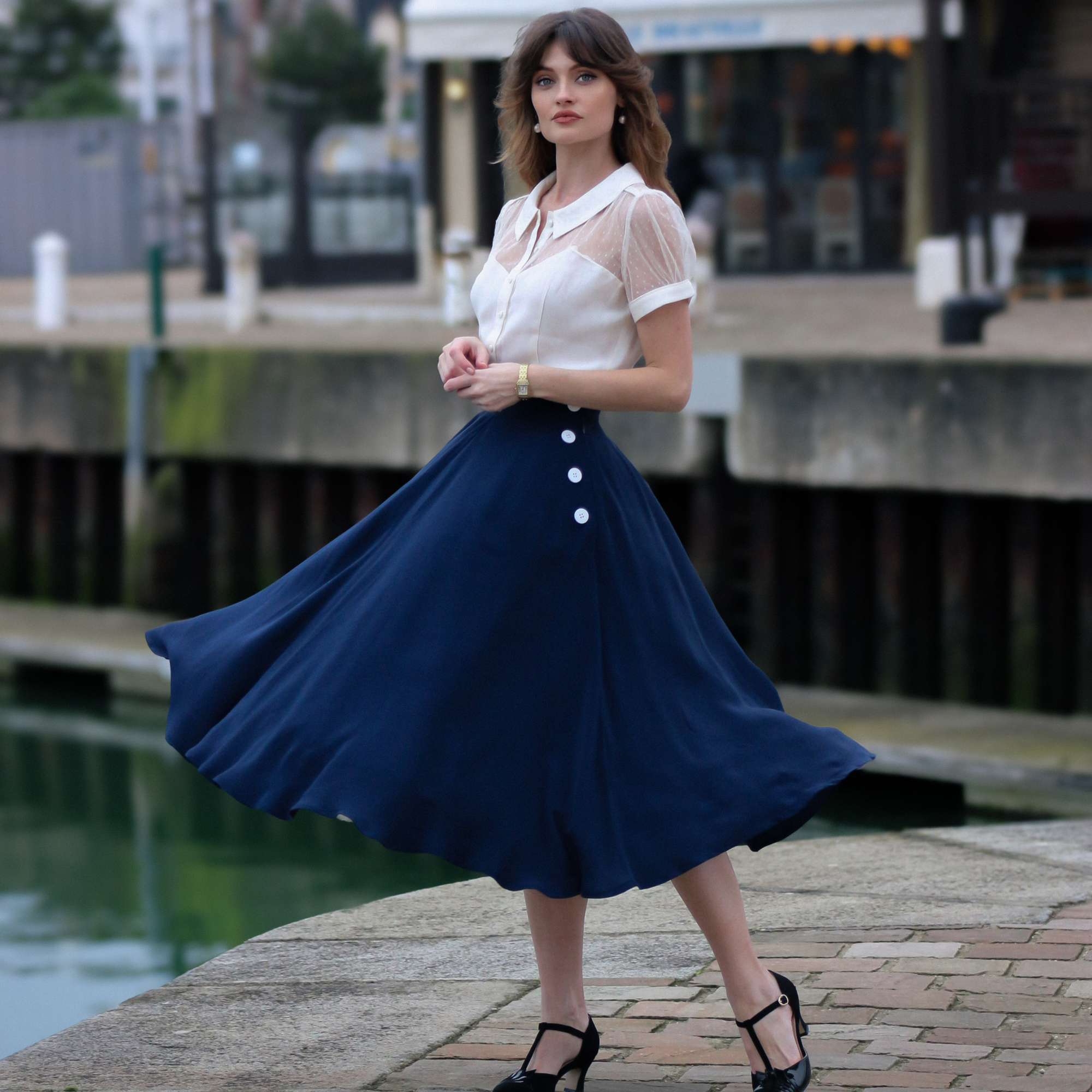 A woman wearing a navy blue swing dance skirt with decorative buttons on the left side, paired with a white top. The skirt swings out in a full circle.